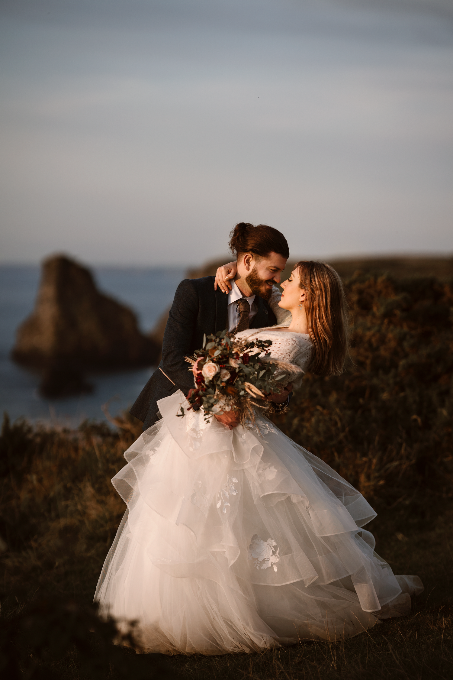 vCouple embracing on a cliffside at sunset during an outdoor wedding portrait by Soft Stories by Angela in Cornwall
