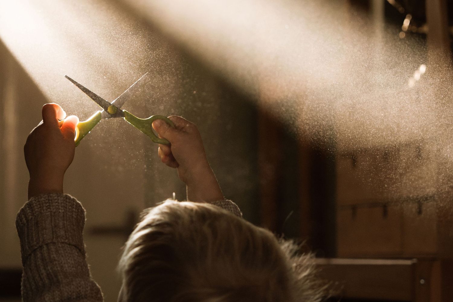 Child holding scissors up toward a beam of light indoors.