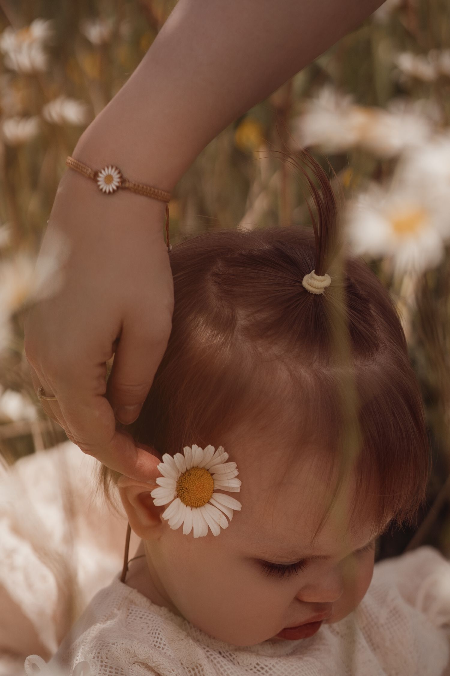 mum placing a daisy flower behind her daughters ear with family photographer Angela from Swadlincote