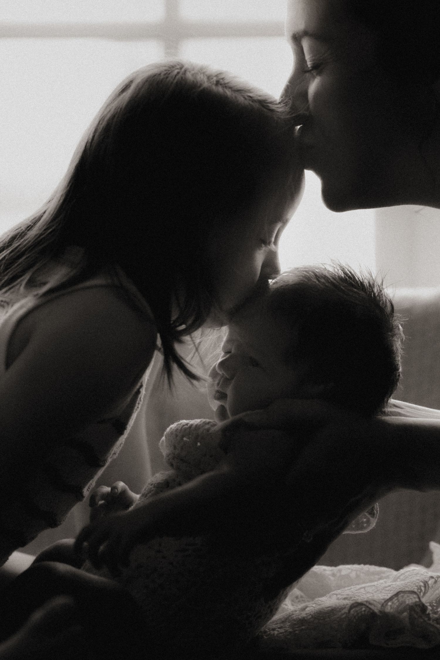 Sister gently kisses her newborn sibling’s head during a quiet family moment at home.