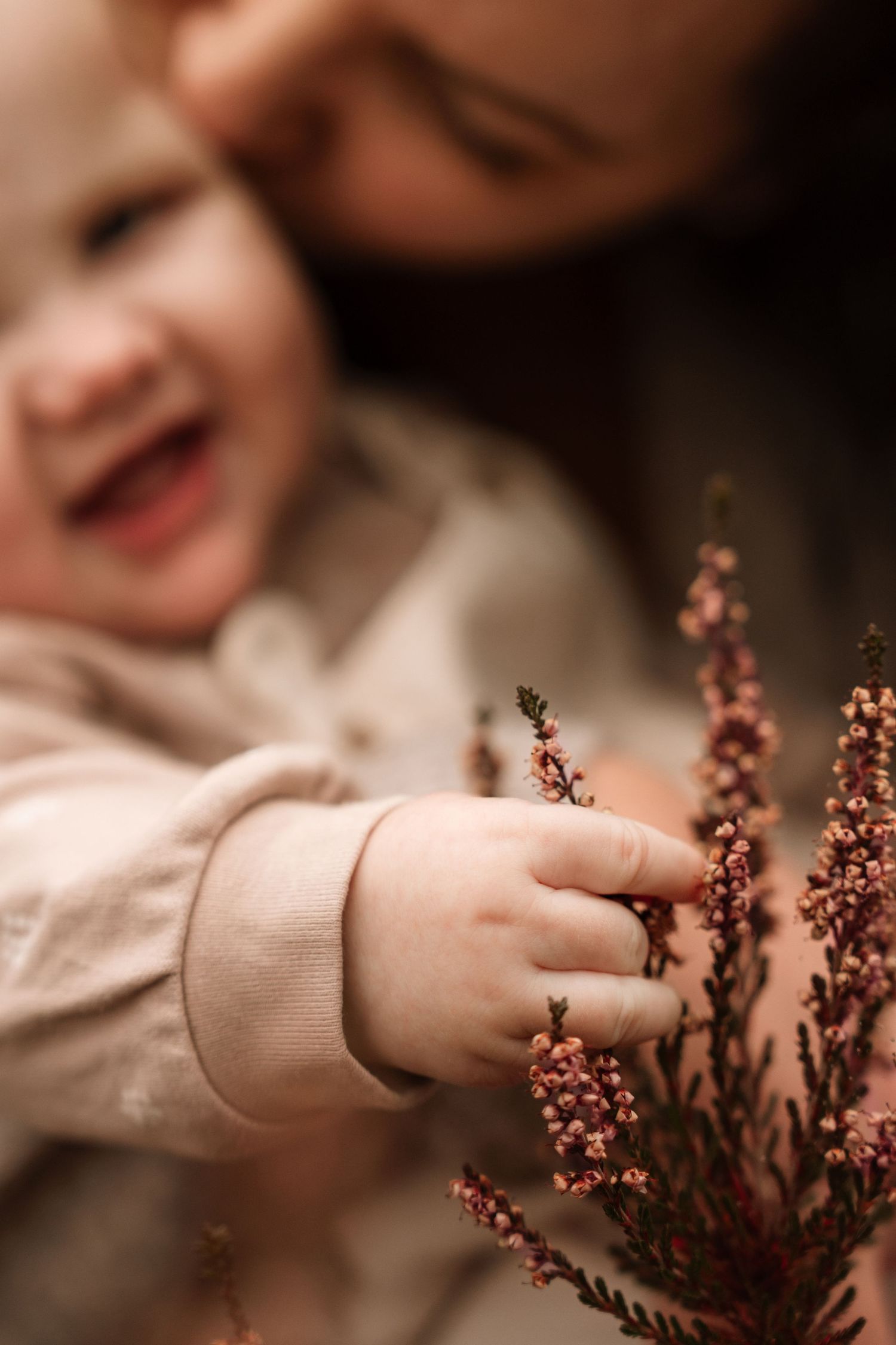 Mother kisses her baby’s cheek as little hands reach for autumn heather during a cozy motherhood session. in Lickey Hills