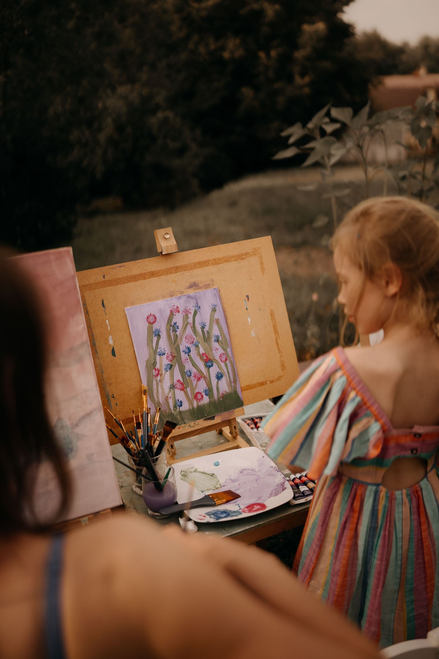 Child paints outside at an easel during a creative storytelling photoshoot in warm evening light in Asby