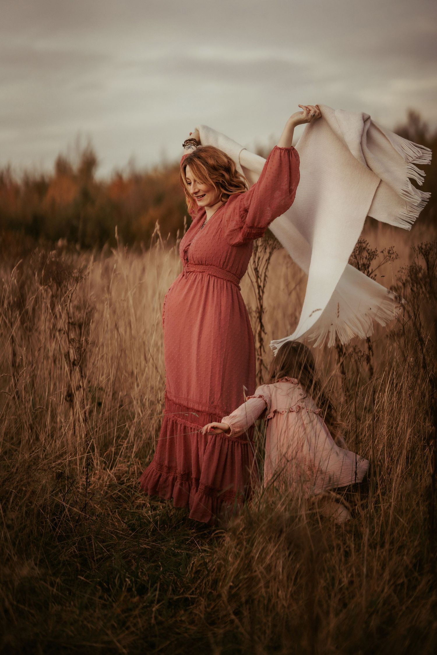 Pregnant parent dancing in tall grass with a child during an outdoor documentary maternity photoshoot in Ashby de la Zouch