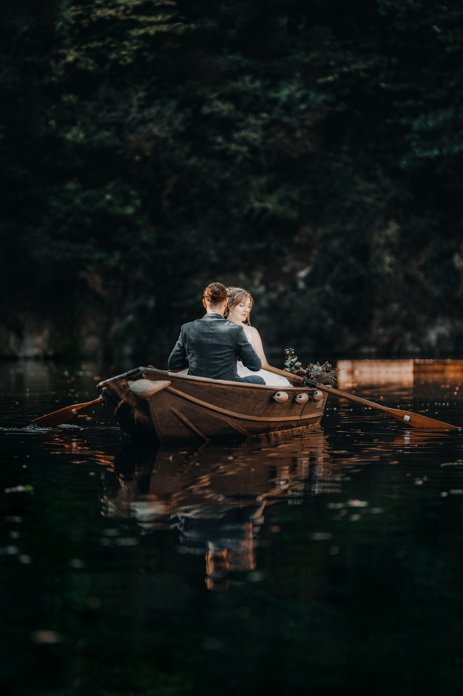 Couple sitting in a boat on still water, embracing during an intimate outdoor wedding session.