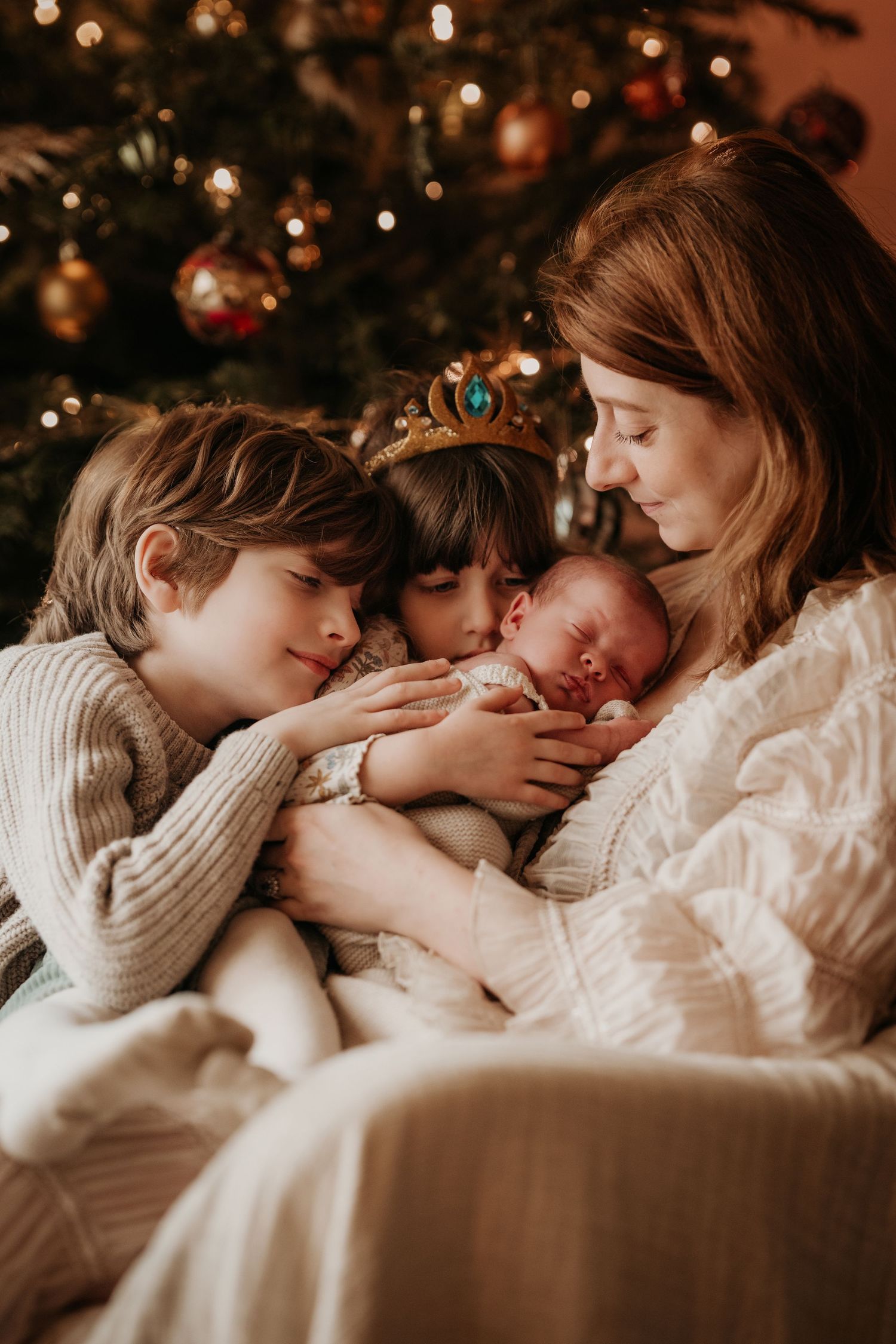 Family gathered around their newborn by the Christmas tree during a warm, at-home lifestyle newborn photoshoot.
