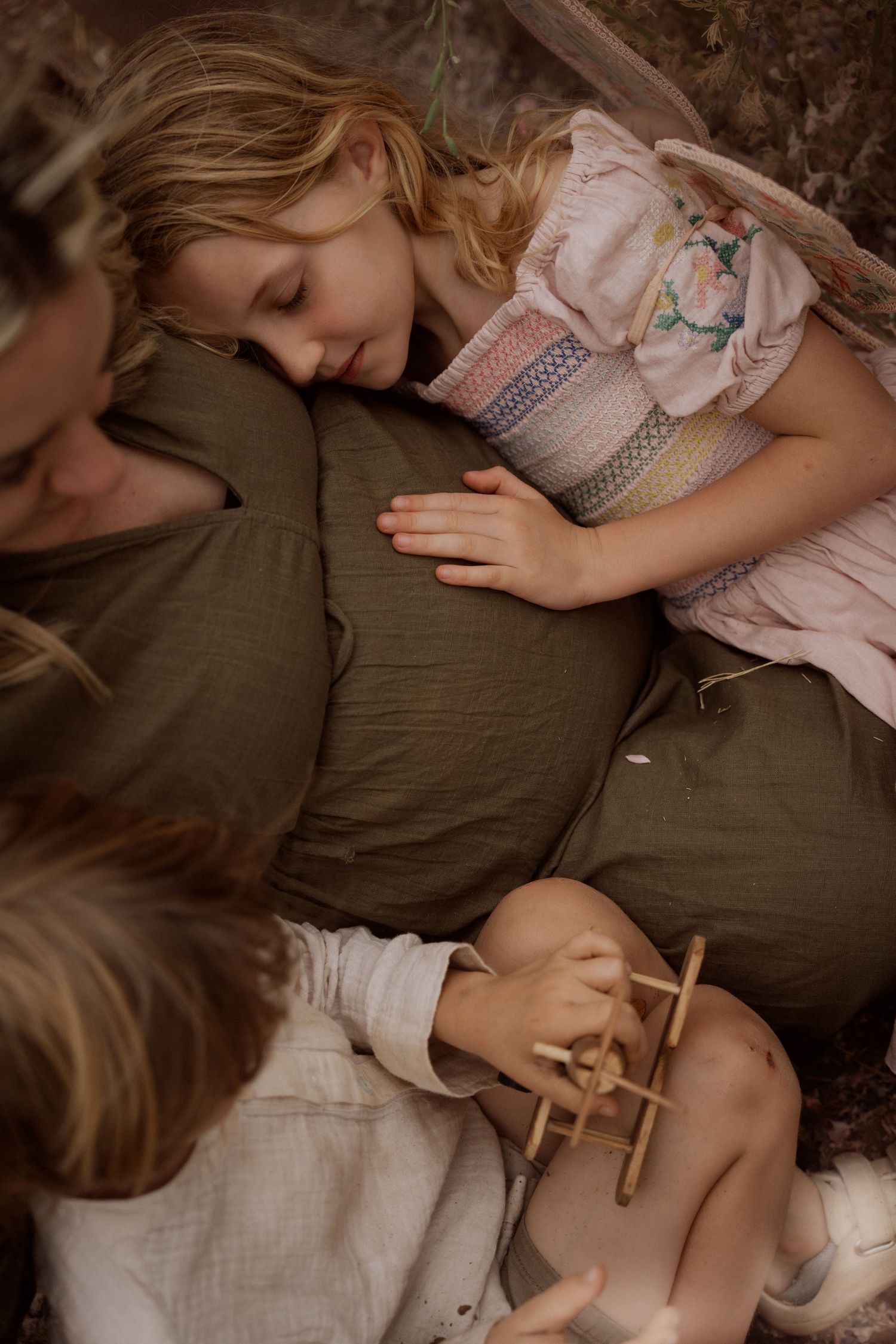 Two children resting on a mum's pregnant belly outdoors, seen from above.