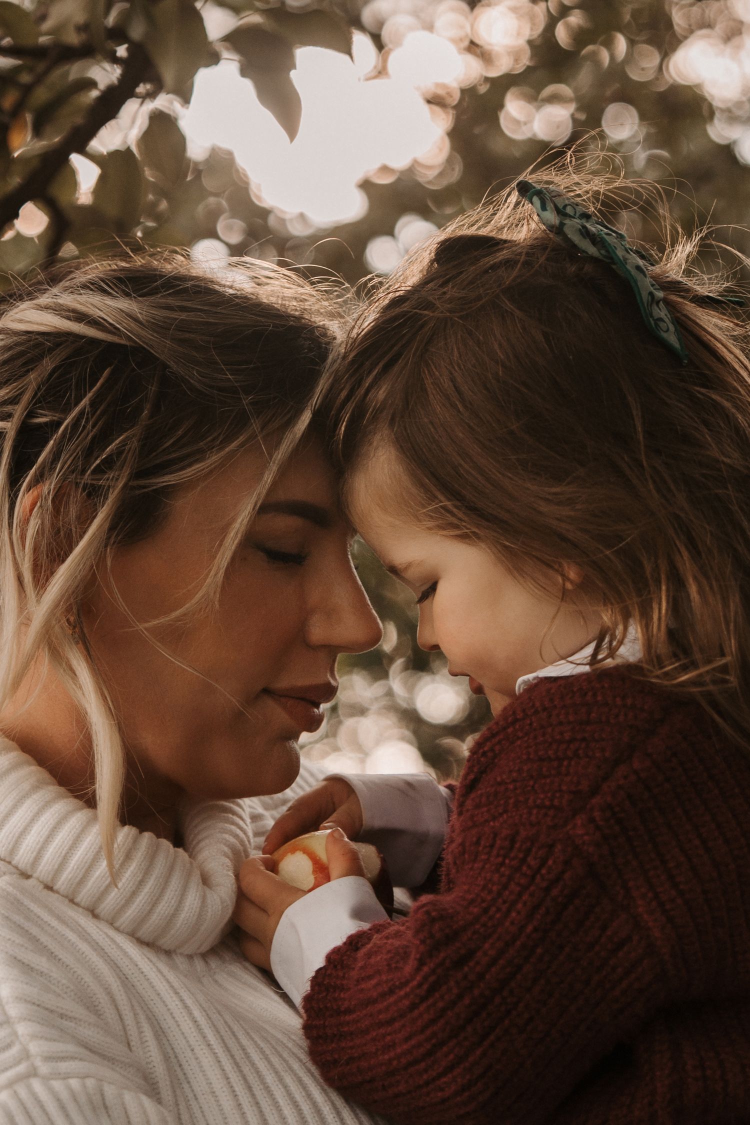 Mother and daughter share a quiet moment among apple branches during a golden orchard shoot in Elford