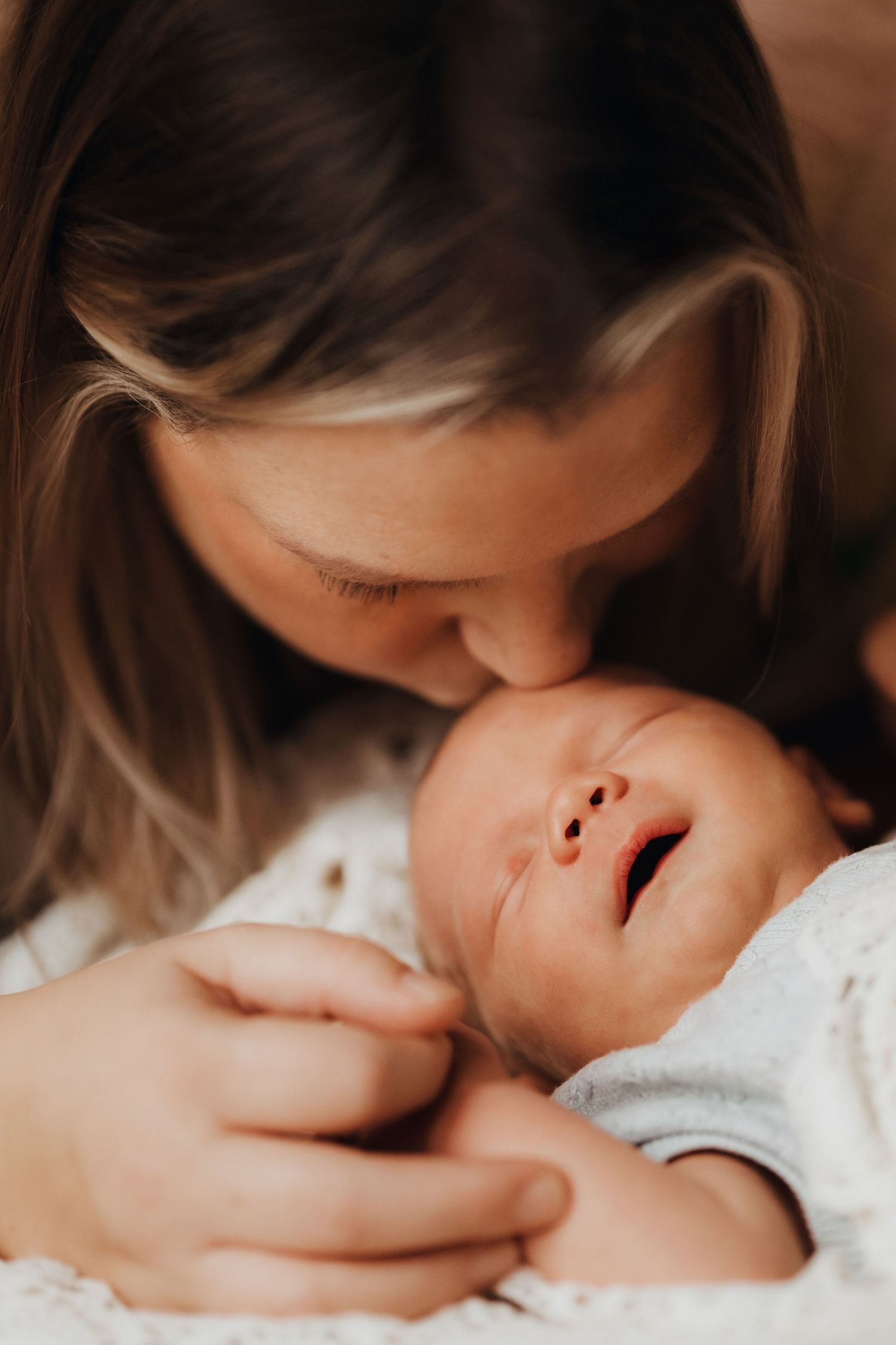 Mother kissing her newborn’s head during a warm natural light lifestyle newborn photography session.