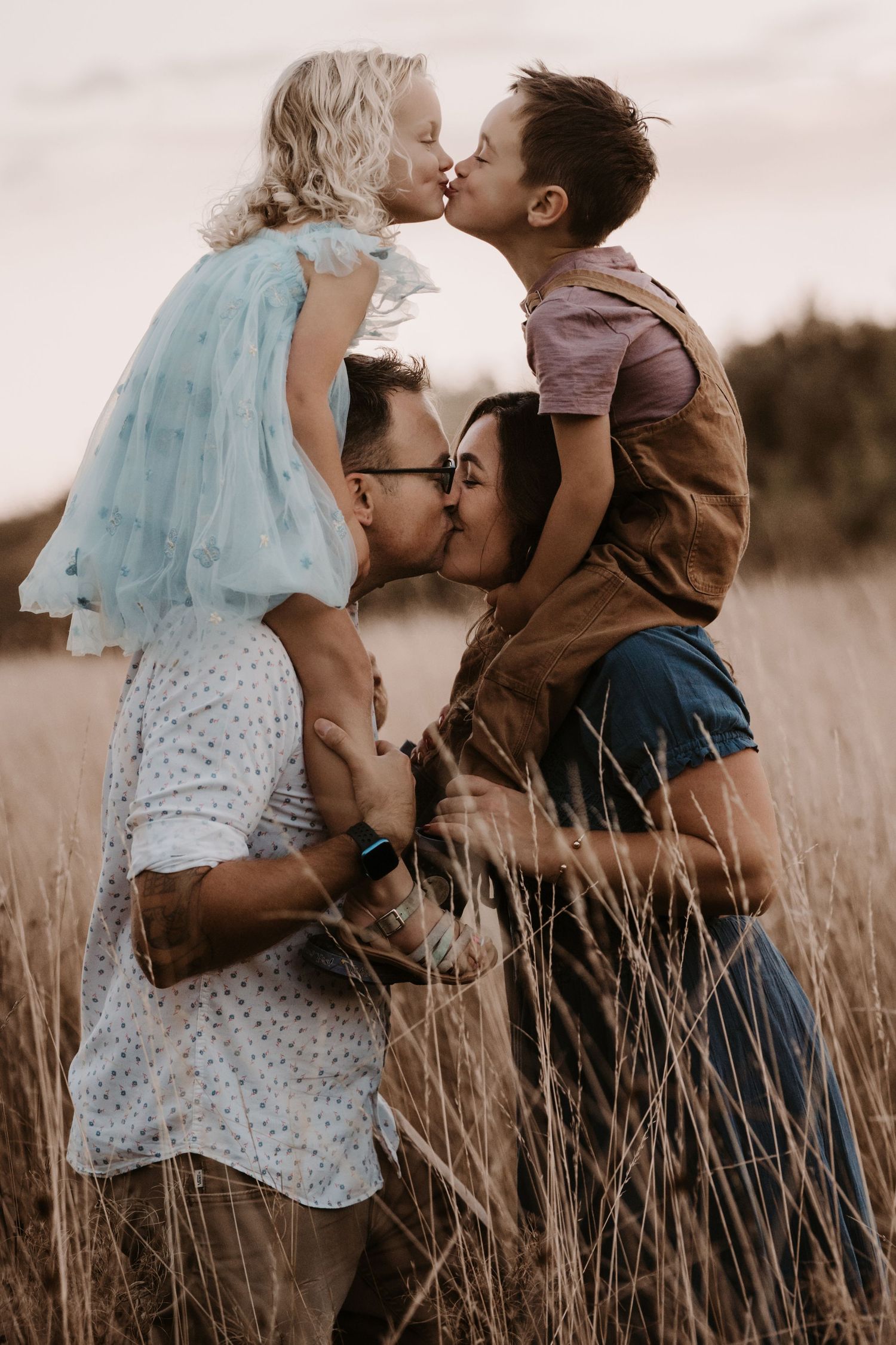 Family shares a kiss in tall golden grass during a playful outdoor photoshoot in the Midlands.