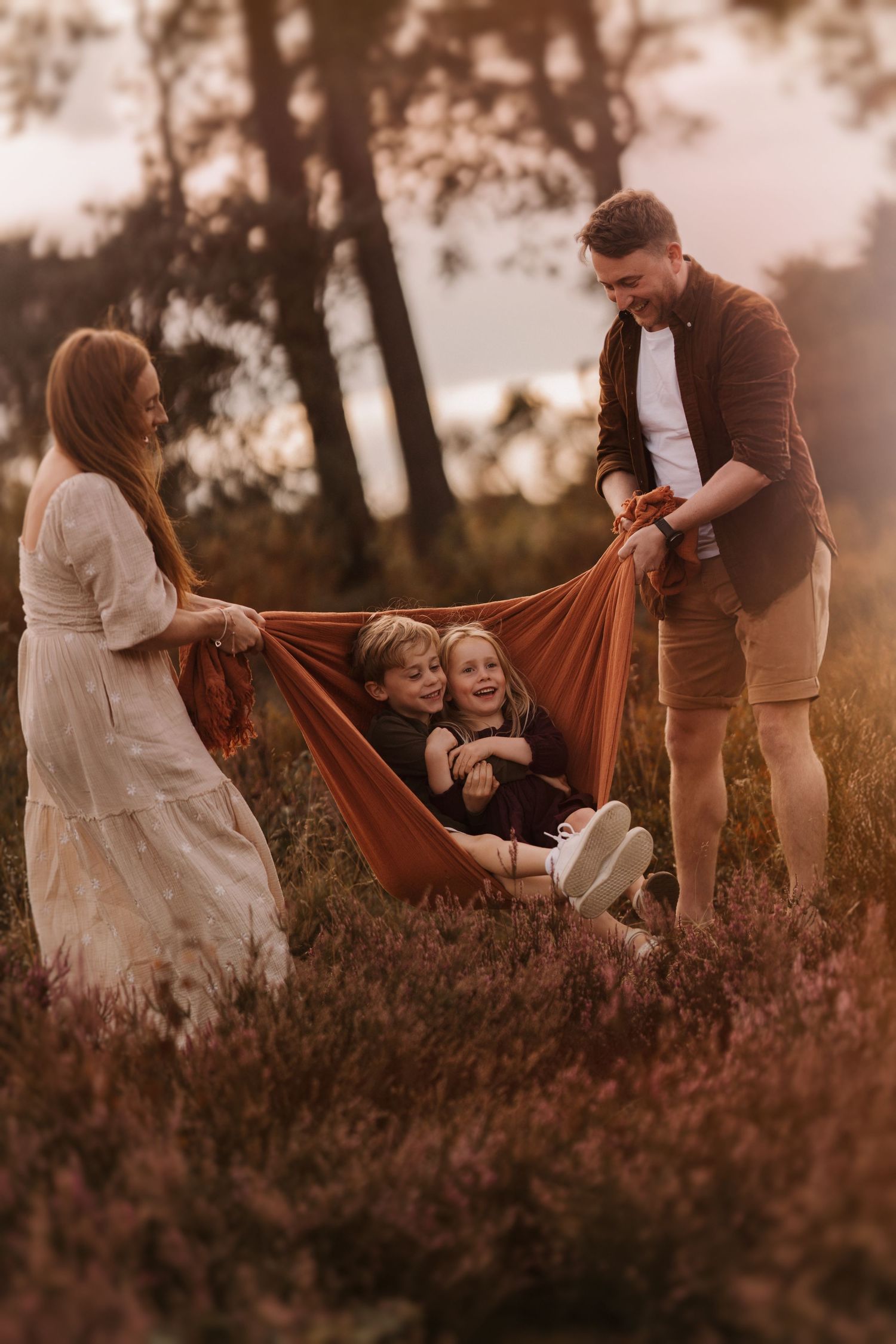 Parents swing their laughing children in a blanket during a golden-hour family storytelling session.