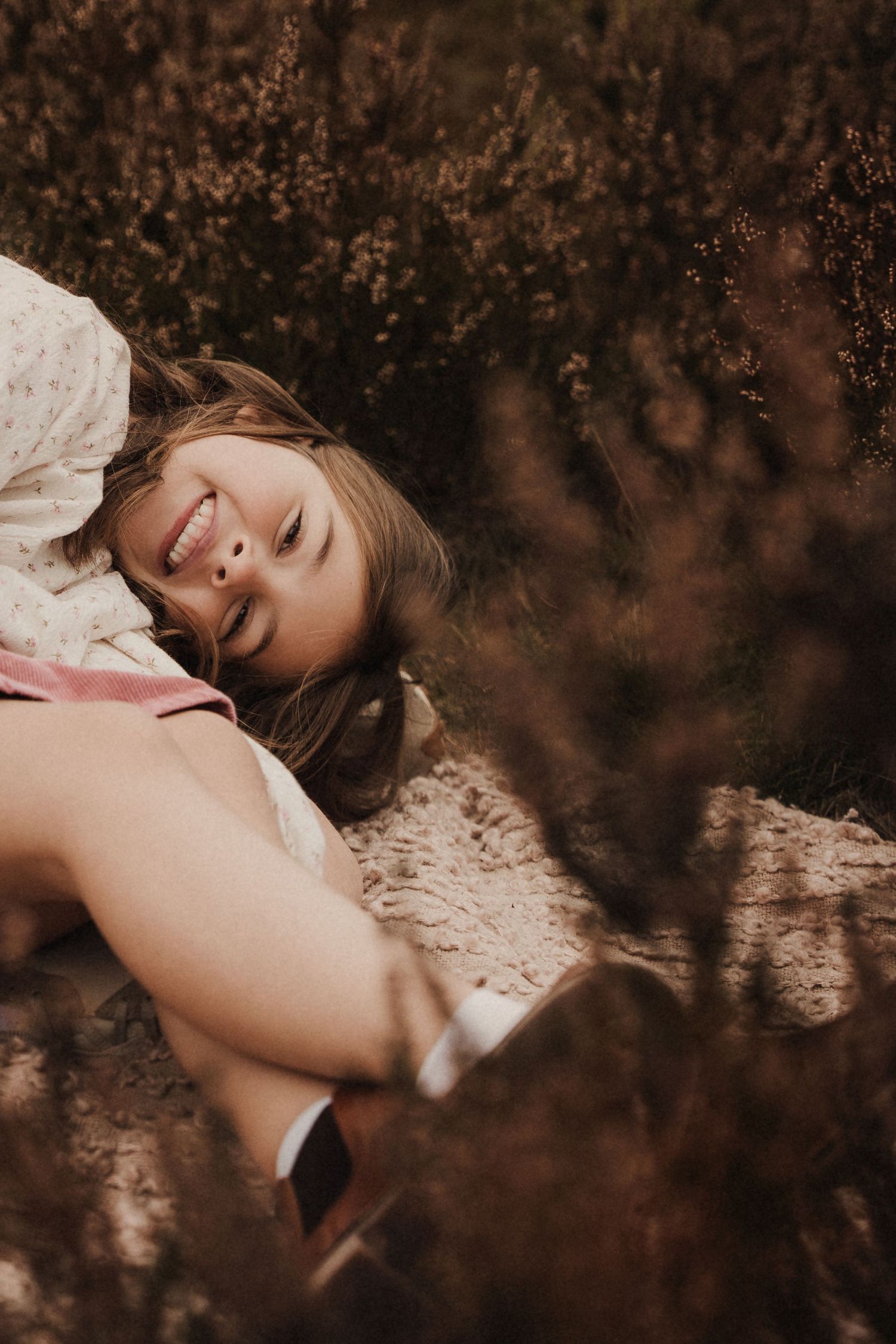 Girl lies in heather field with a gentle smile during a cozy autumn storytelling photoshoot with Alalals Photography