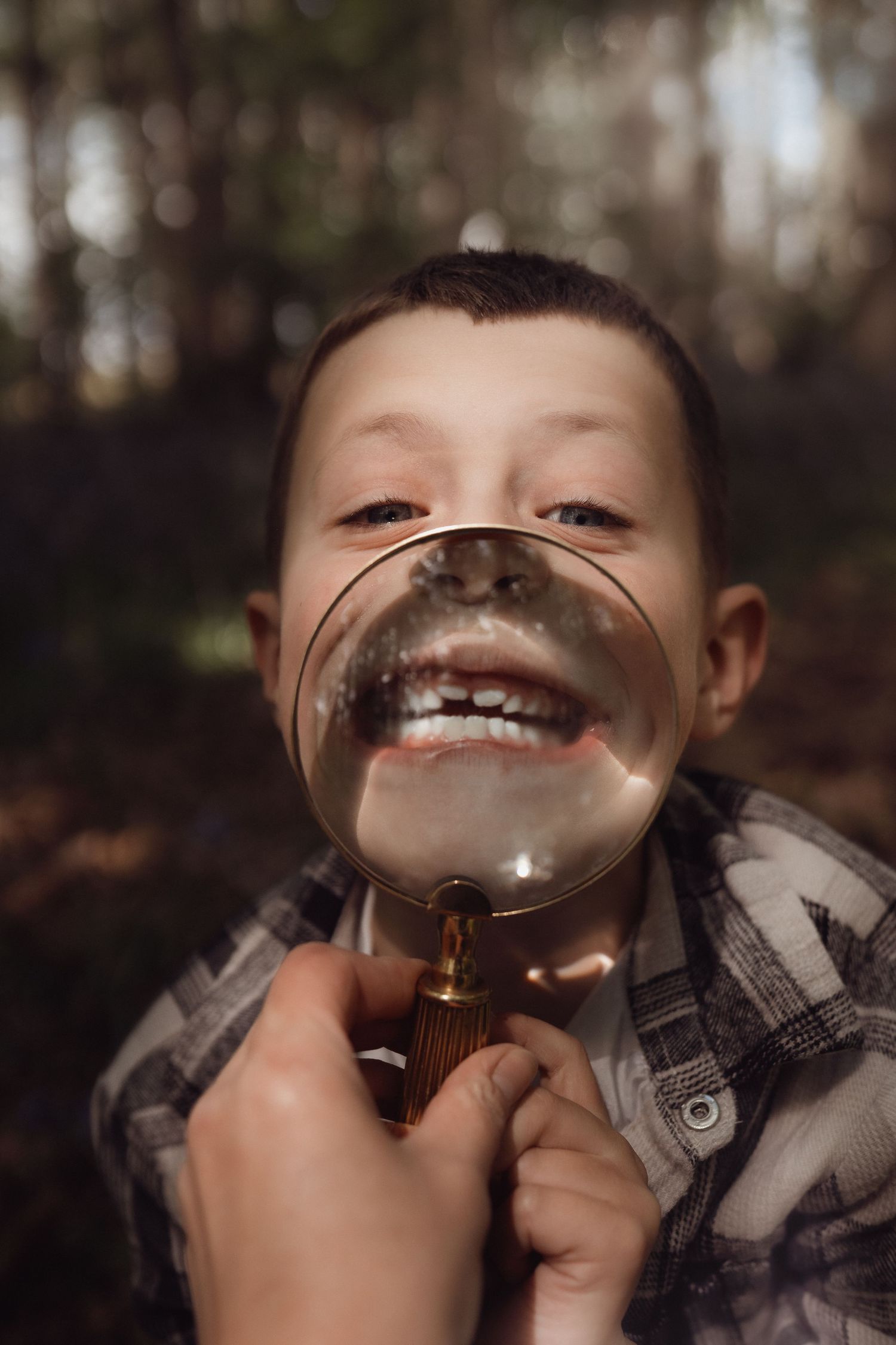 Boy laughs through a magnifying glass during a playful woodland Bluebells family photoshoot in the Midlands.