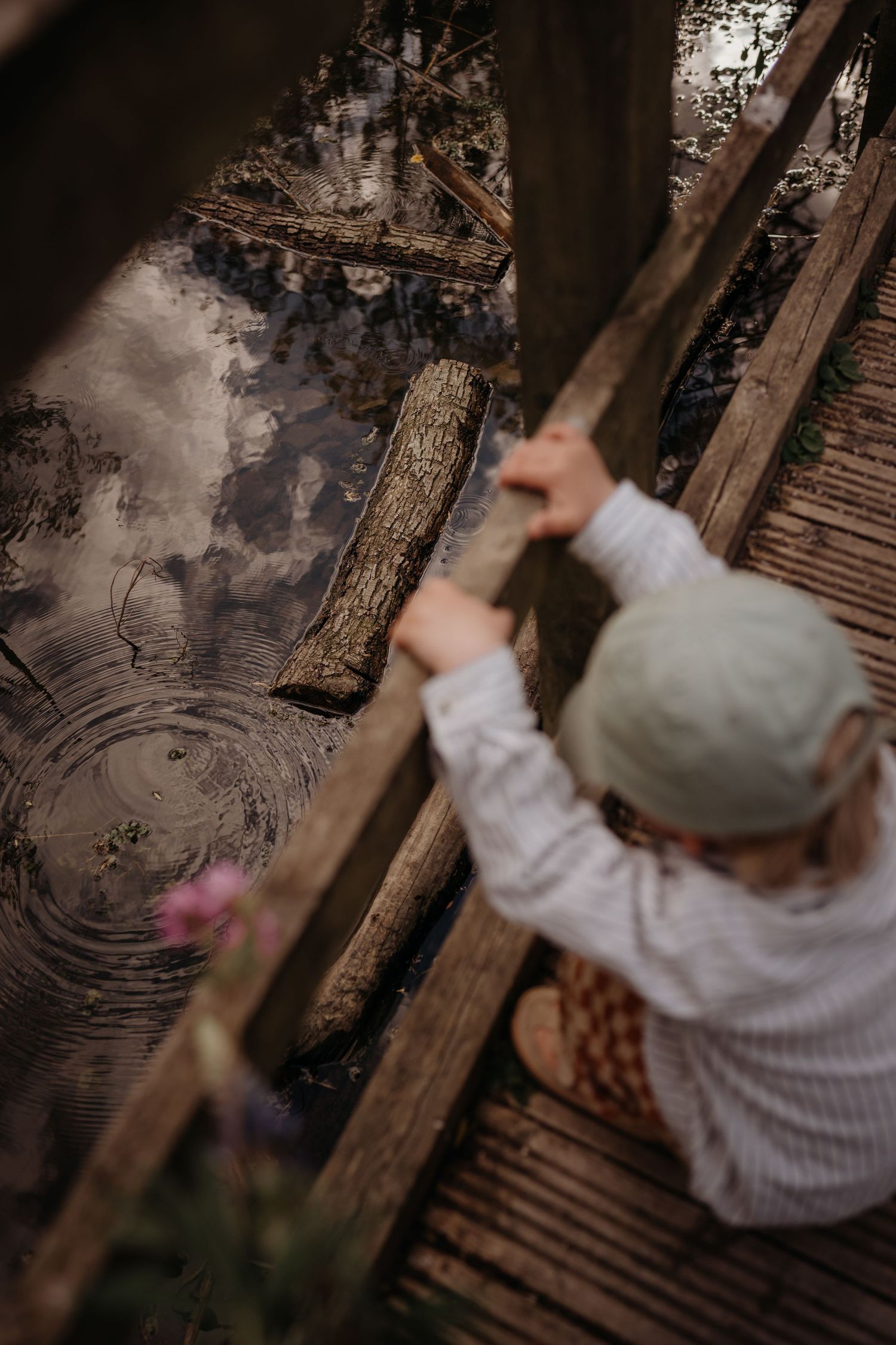 Child leans over a wooden bridge watching the pond below during a natural outdoor family photoshoot in Moira Furnance