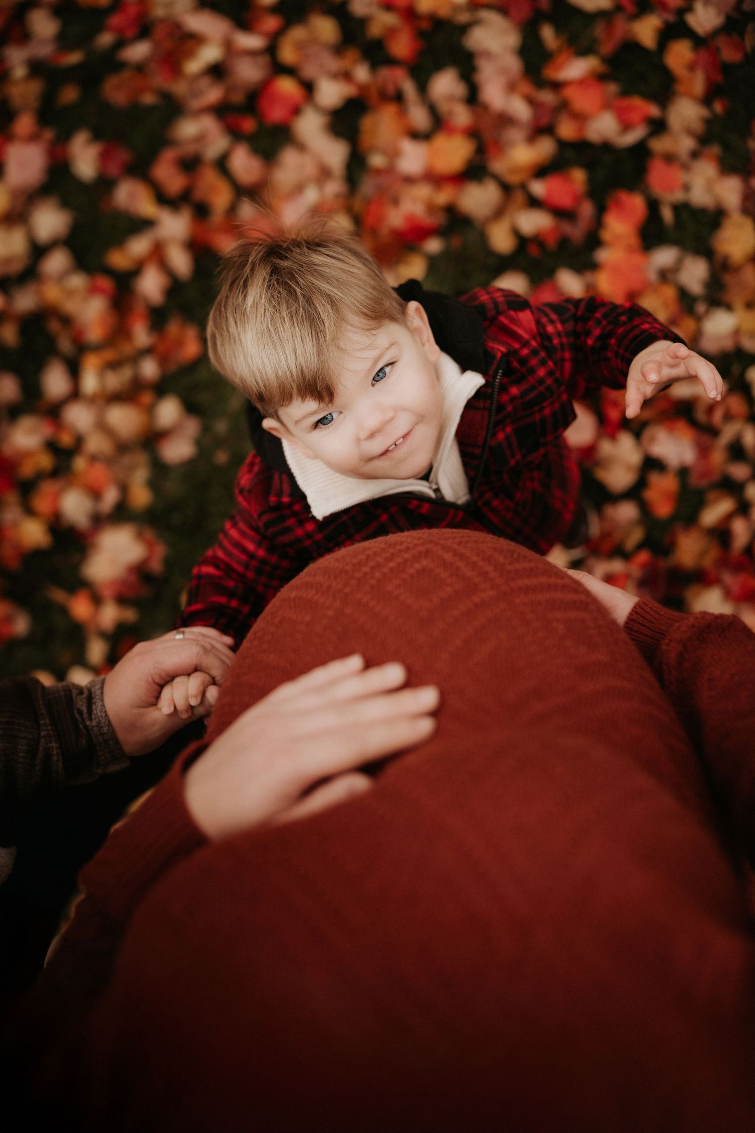Child resting on a pregnant belly during an outdoor documentary maternity session with warm autumn colours.