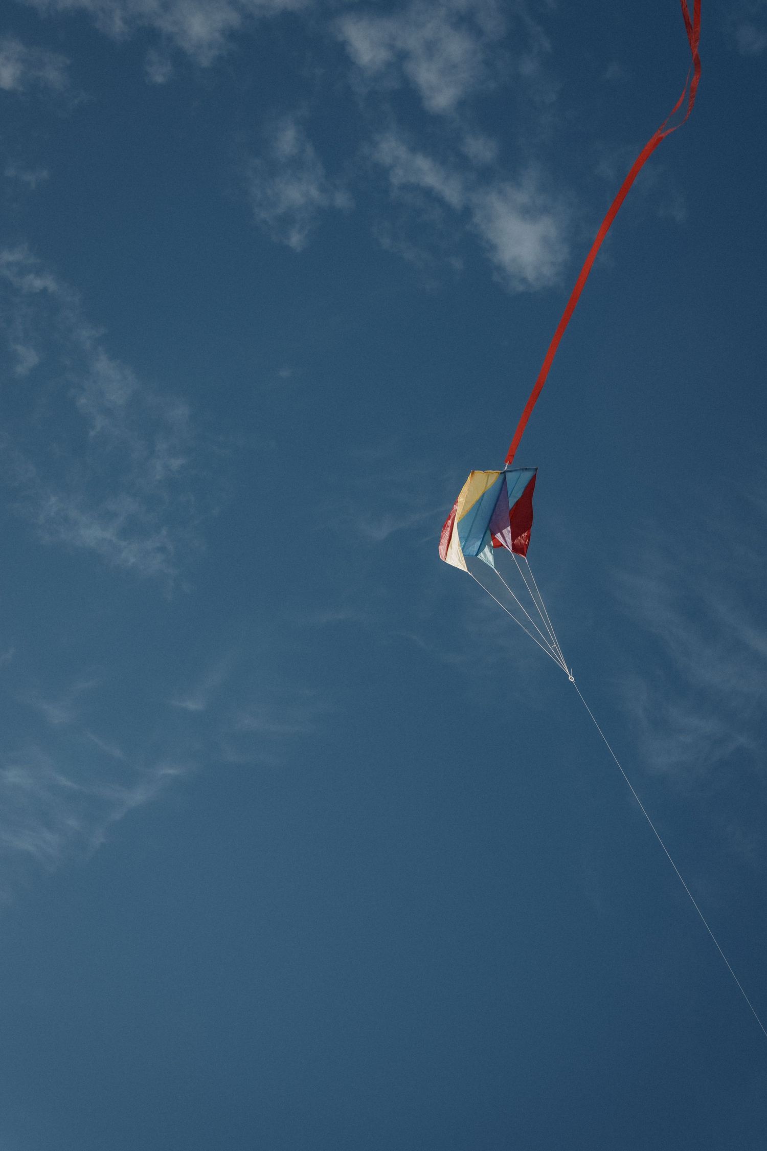 Colourful kite soars high in the blue sky during a playful seaside storytelling photography session.