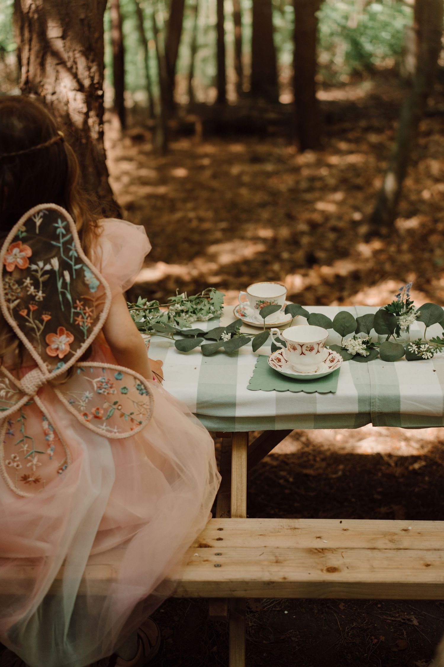Girl dressed as a fairy sits at a woodland table set for a magical outdoor play-inspired birthday photoshoot at Little Wildlings Natureplay
