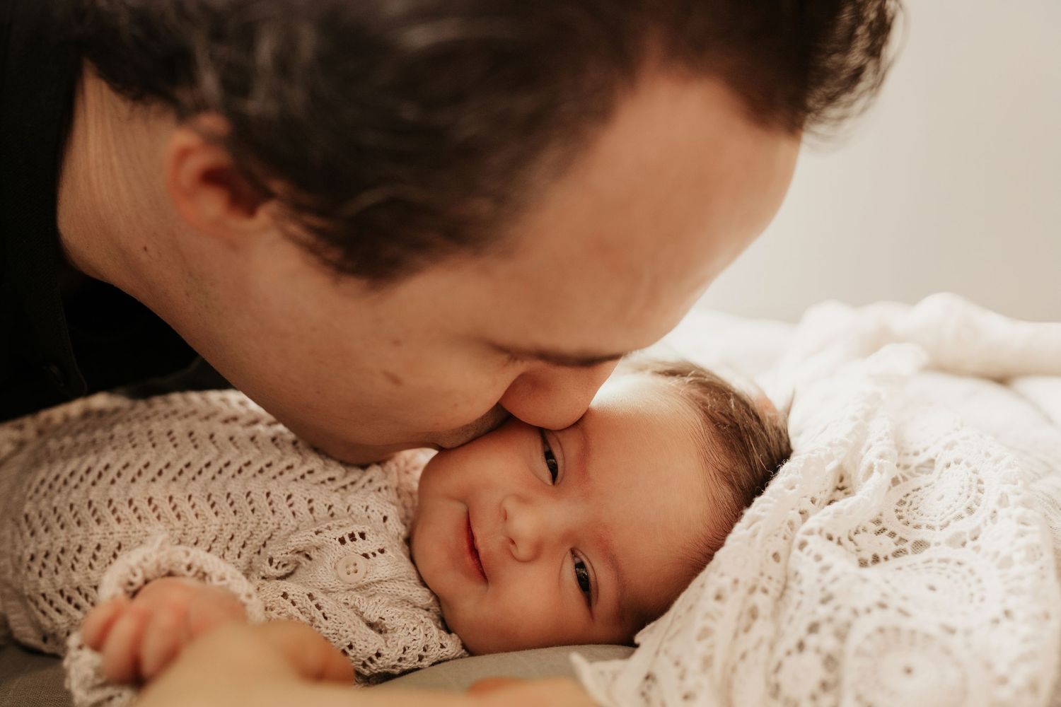 Father kissing his newborn’s cheek as the baby smiles softly, captured during an intimate lifestyle newborn photoshoot in Stoke on Trent