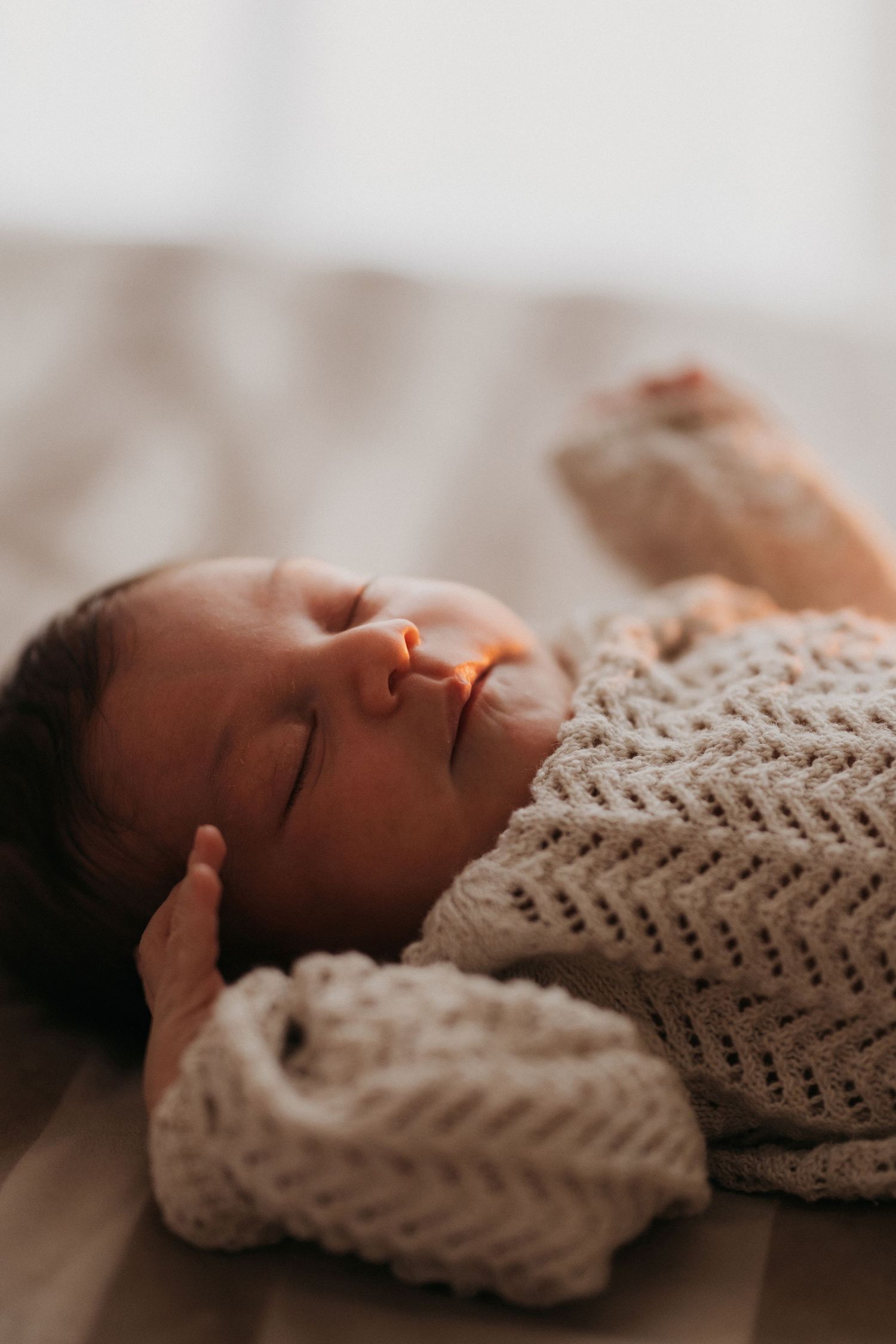 Newborn sleeping peacefully in a knitted outfit during a natural in-home photoshoot.