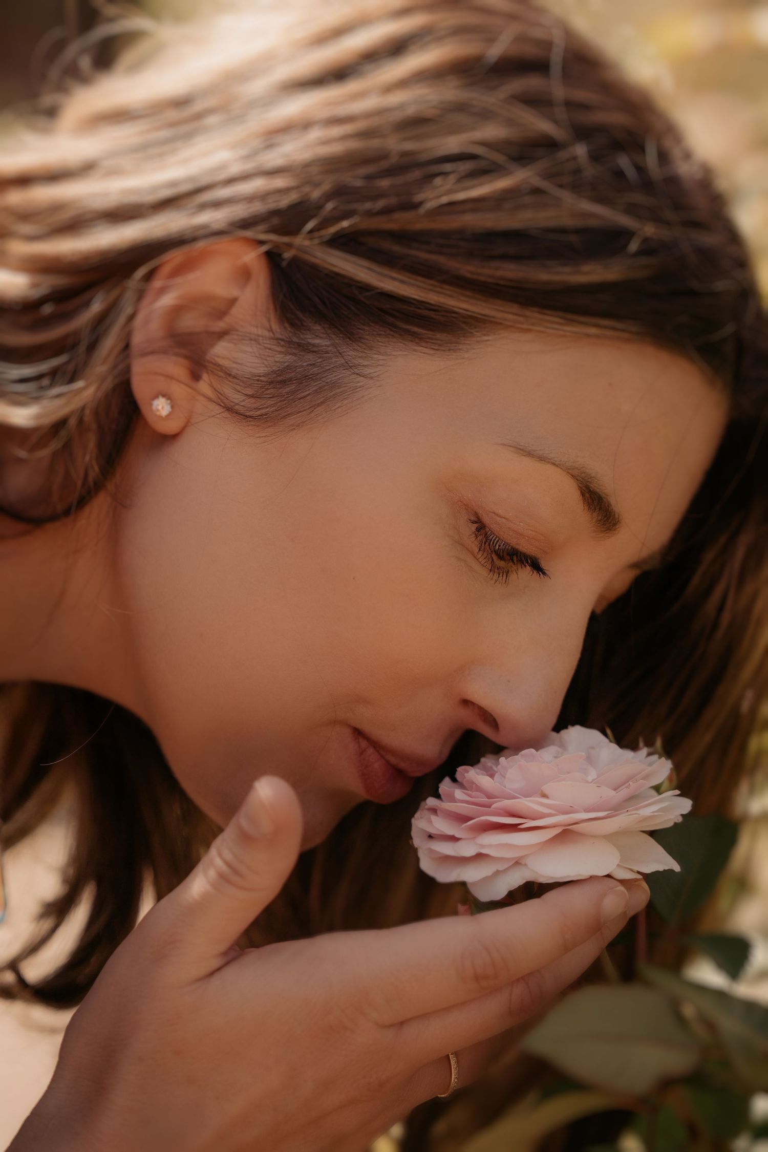Soft portrait of a woman closing her eyes as she smells a pink flower – calm, feminine photography capturing quiet joy.
