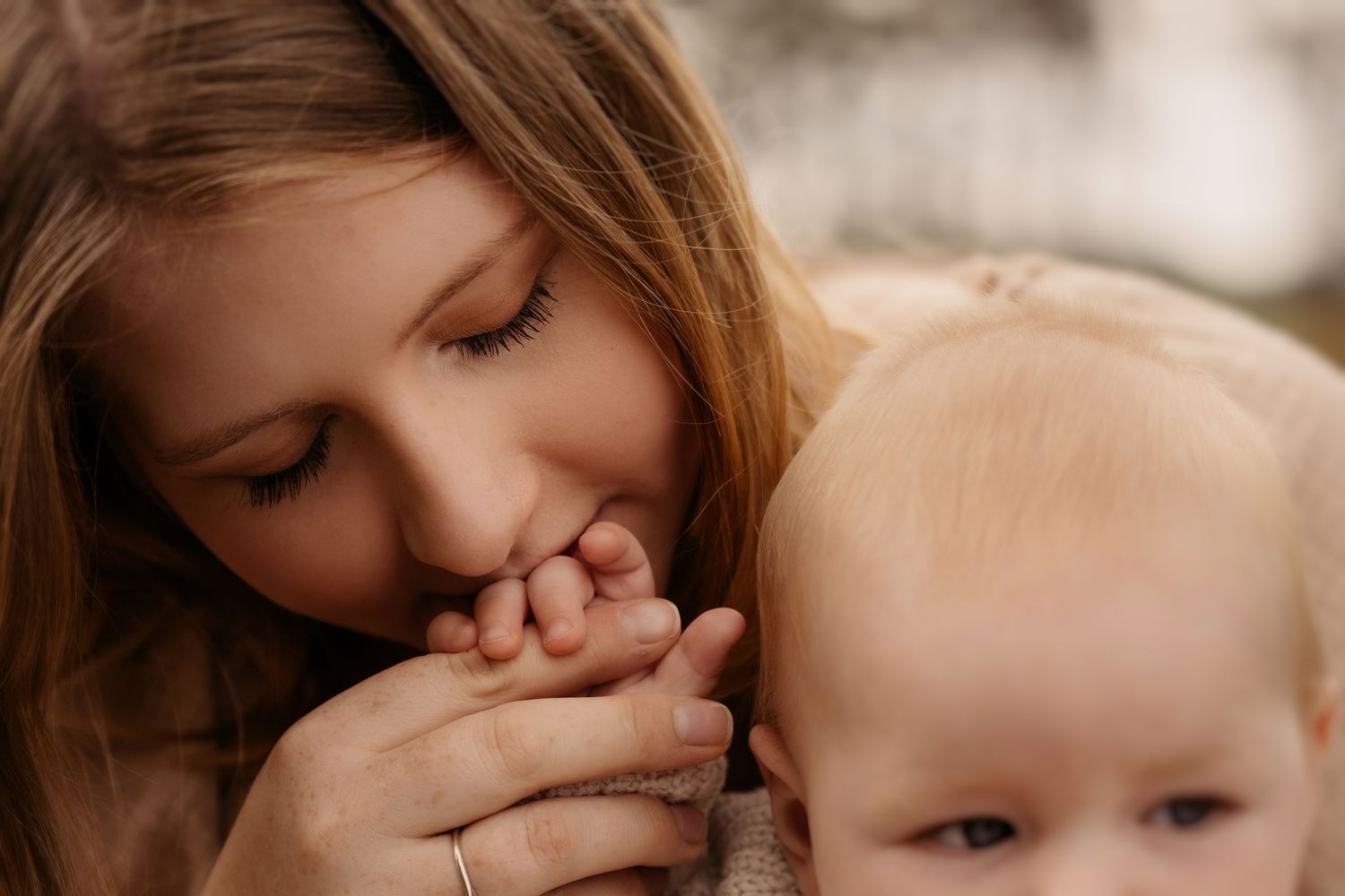 Older child gently kissing a baby’s hand, both close together, captured in a soft, intimate moment of sibling connection