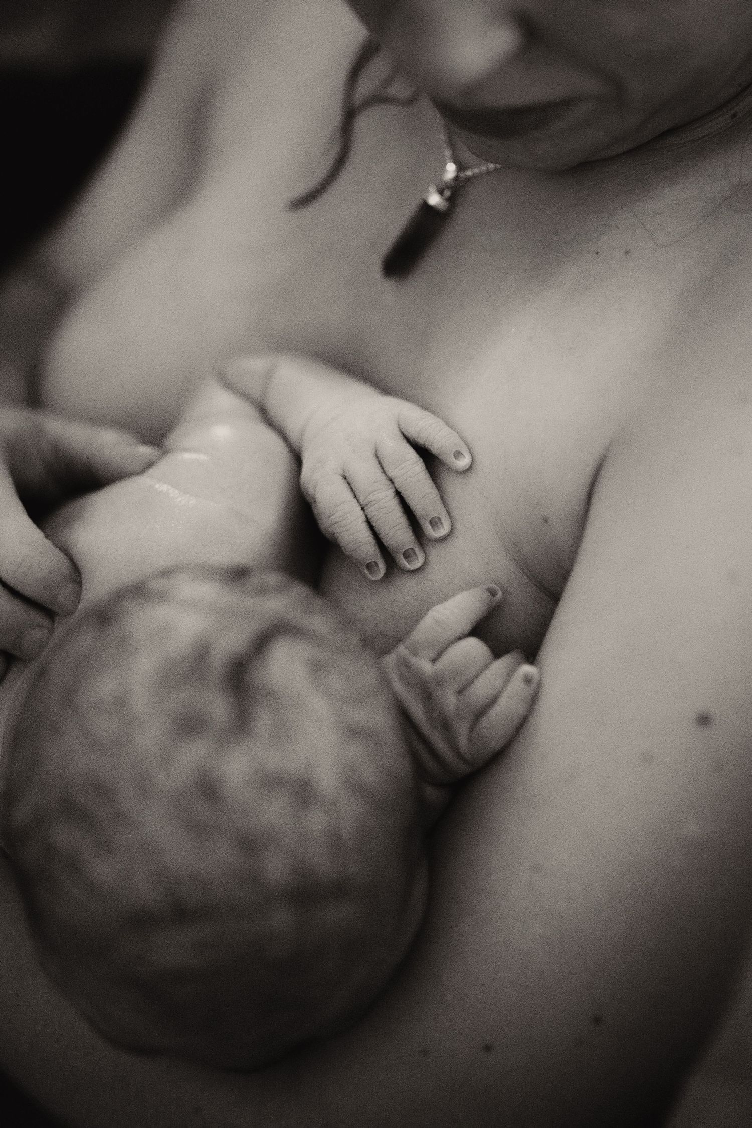 Newborn held skin-to-skin in a birth pool during a documentary water birth photography session.