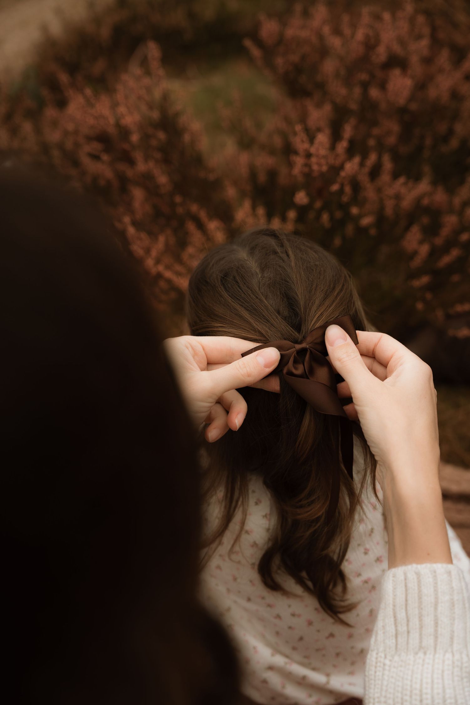 Mother braids her daughter’s hair during a tender outdoor motherhood photoshoot in Birmingam, Lickey HIll