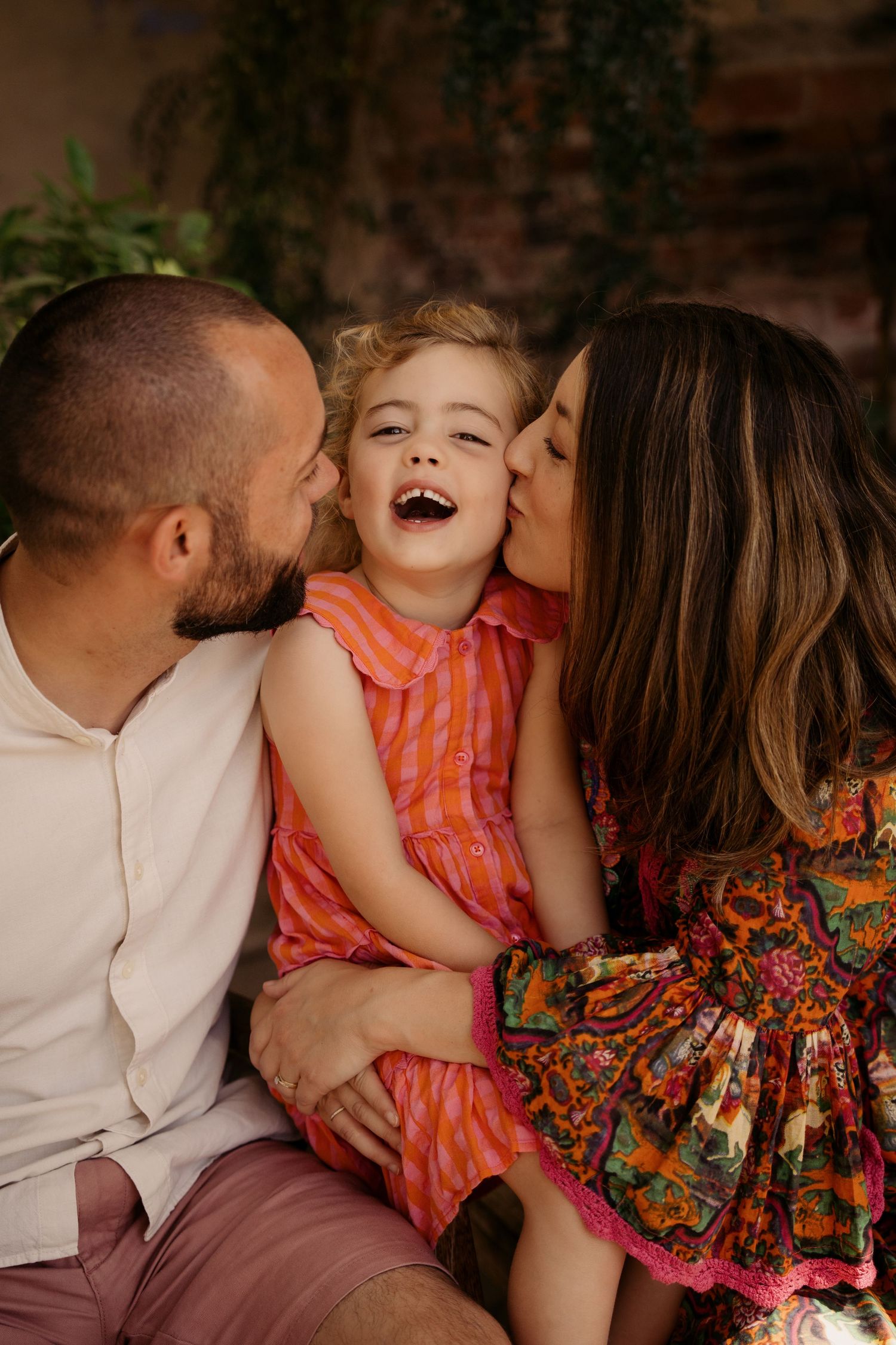 Parents kissing their child during a joyful lifestyle family photography session with warm natural light.