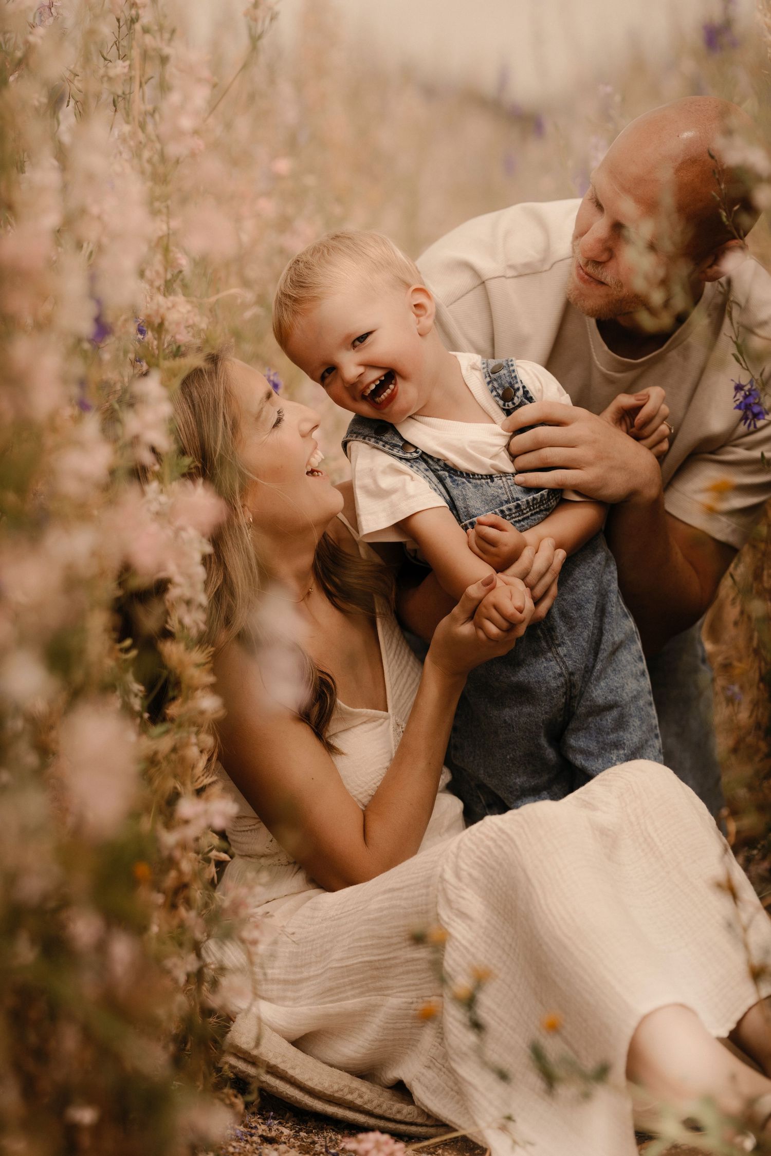 Parents laughing with their child in a flower field during a joyful outdoor documentary family photoshoot in Confetti Field
