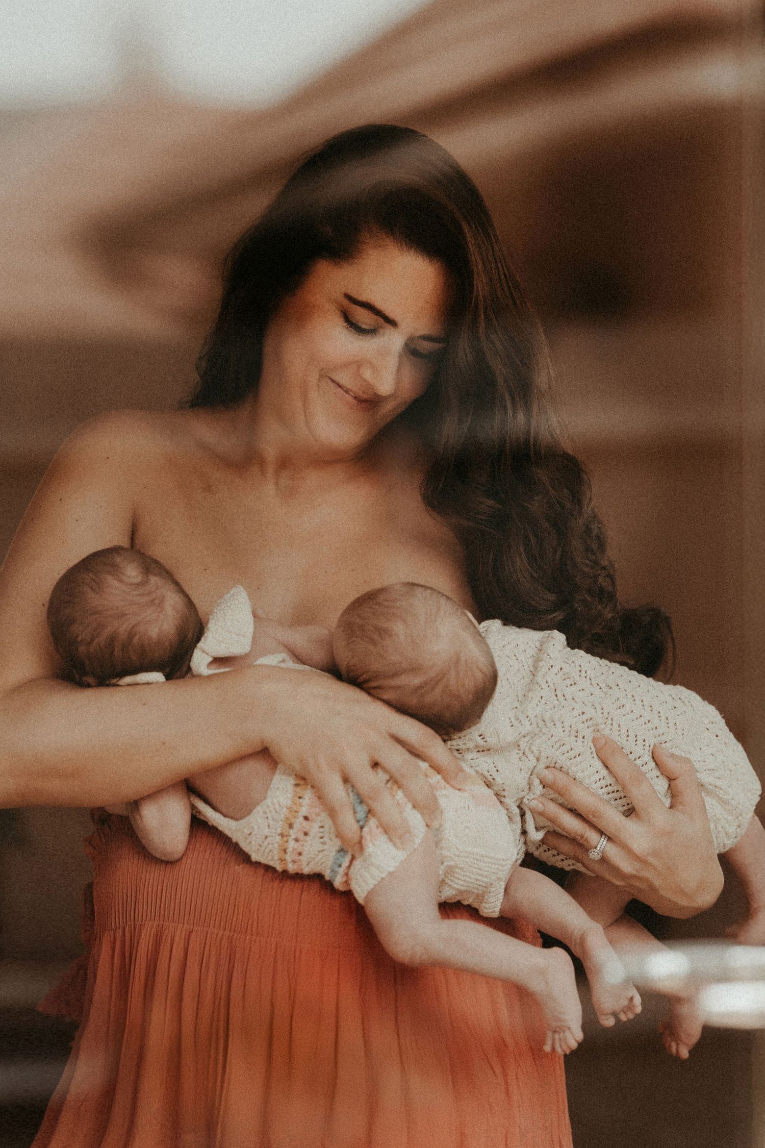 Mother holding her newborn twins close, an intimate breastfeeding moment documented in a natural storytelling photoshoot.