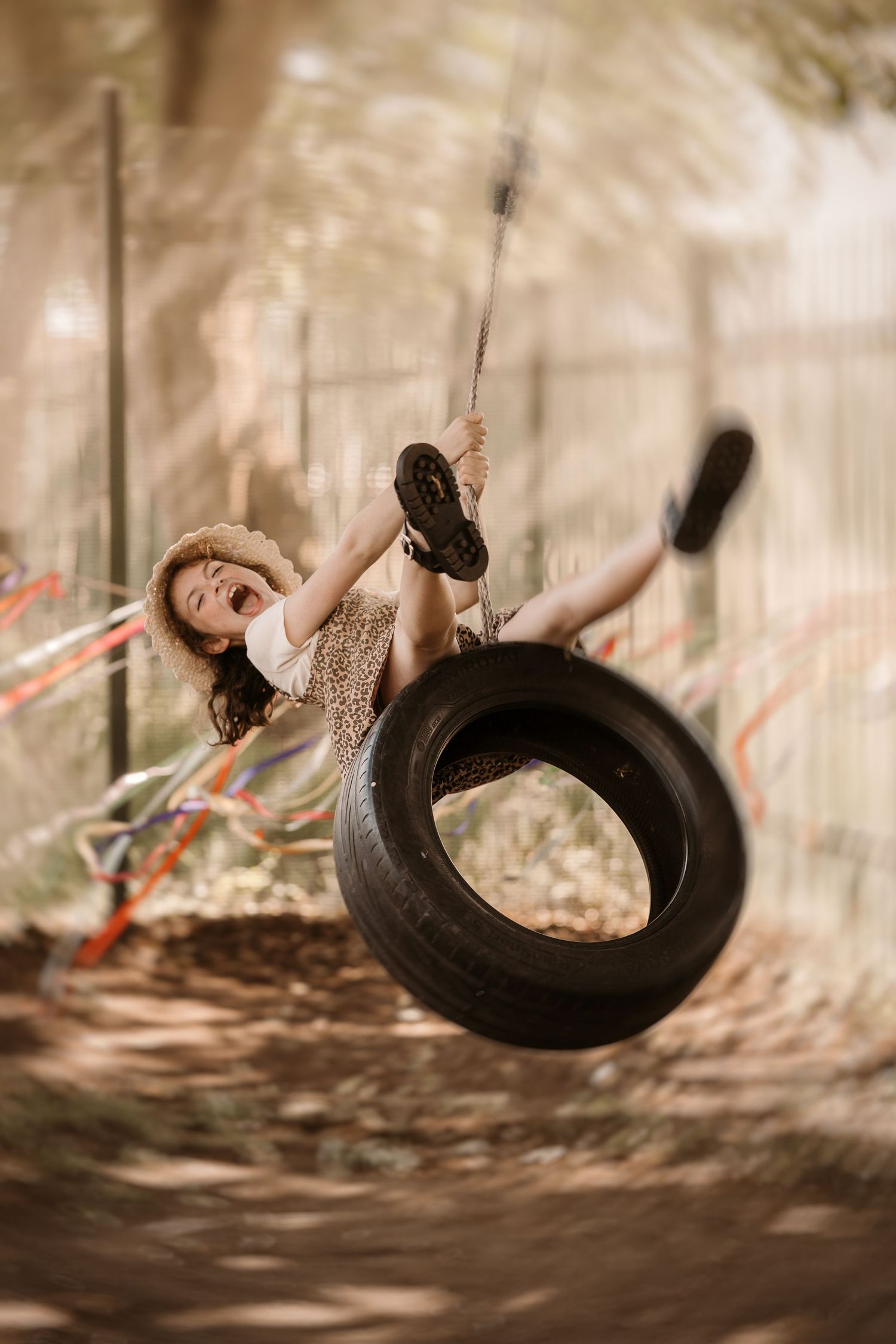 A child swings on a hanging tyre in a woodland clearing, legs lifted mid-air, laughter frozen in warm, dappled light.