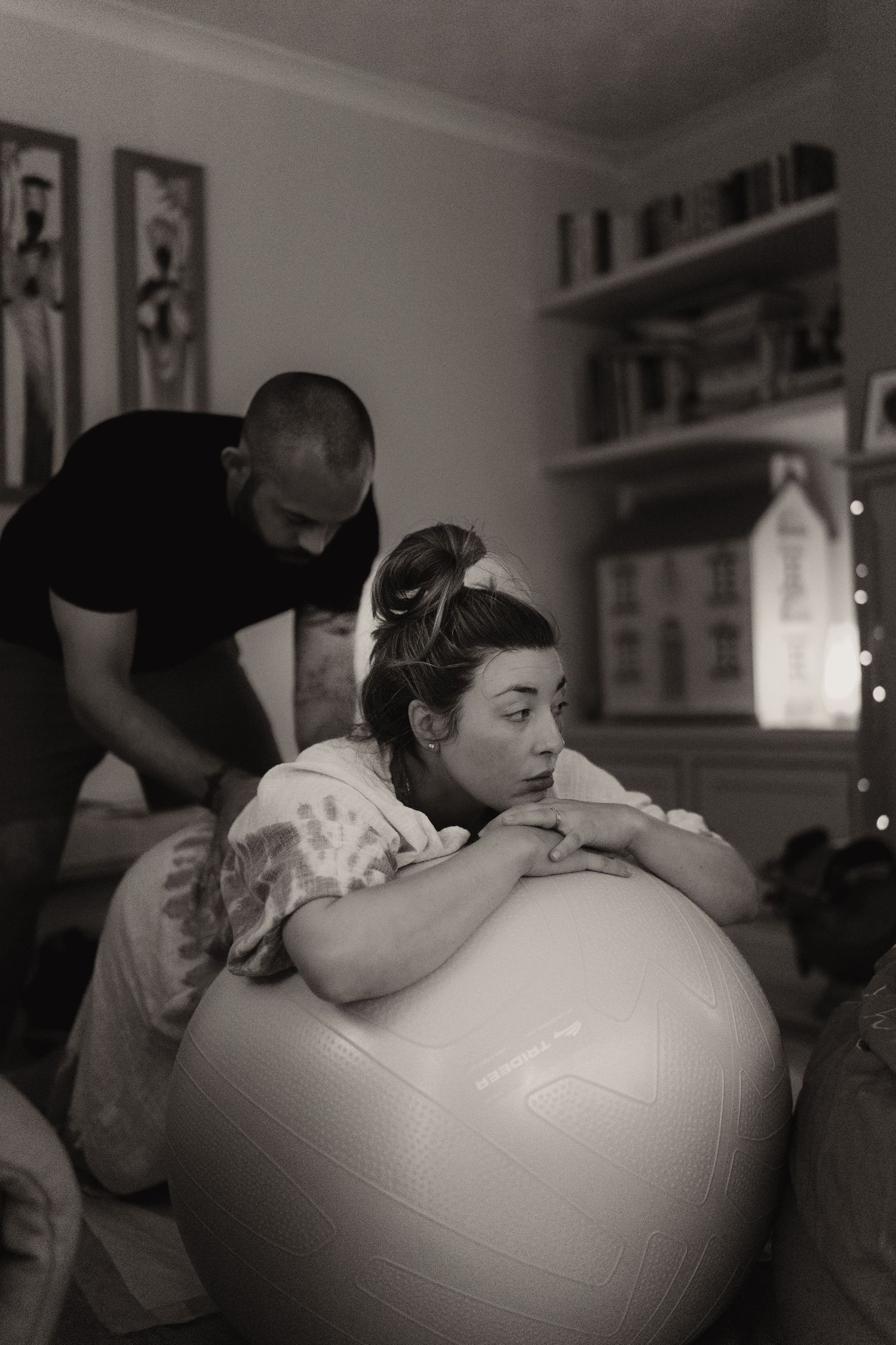 Support person comforting a laboring parent leaning on a birth ball during an intimate home birth by Soft Stories by Angela