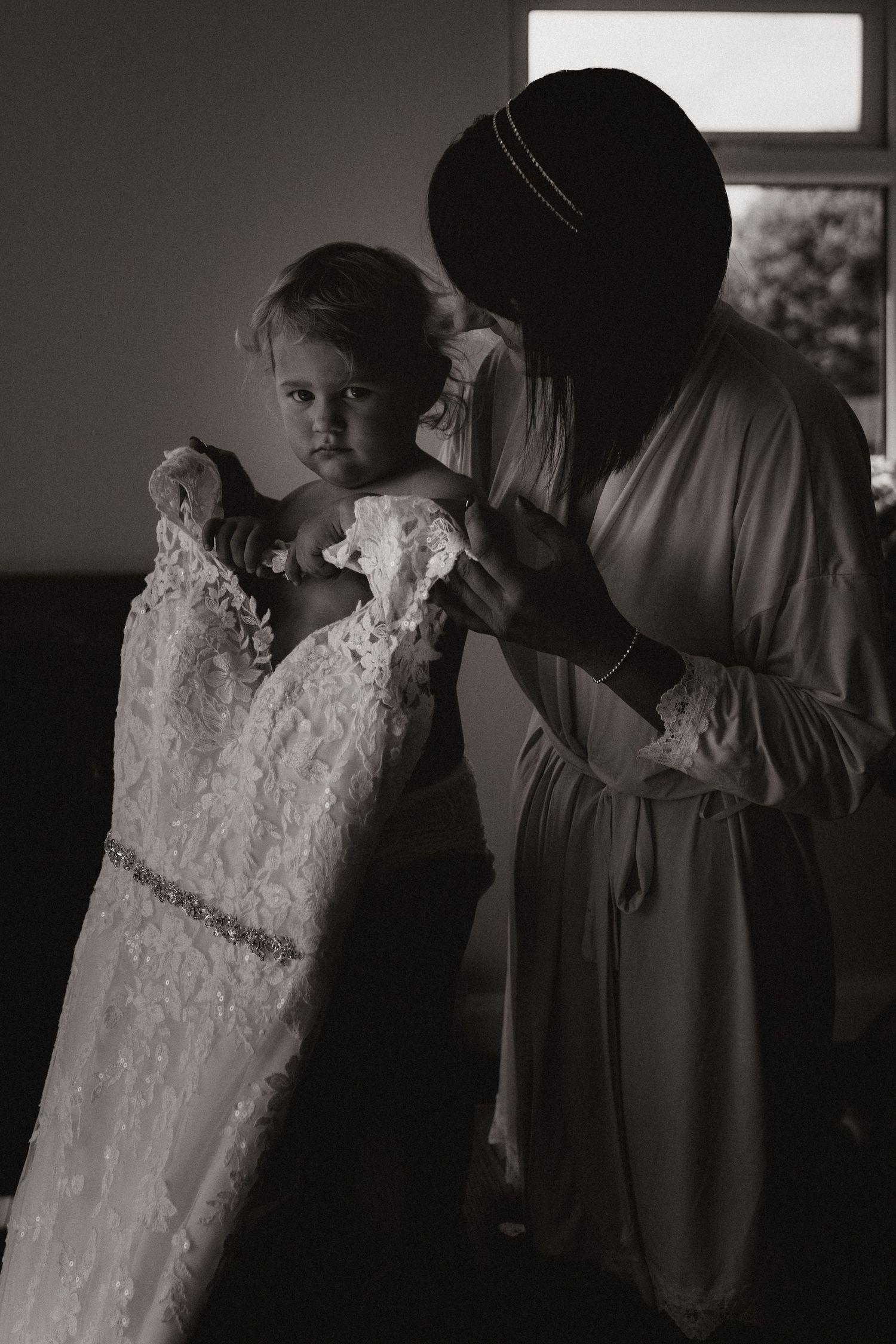 Bride and her baby share a quiet moment while preparing the wedding dress during a candid morning shoot.