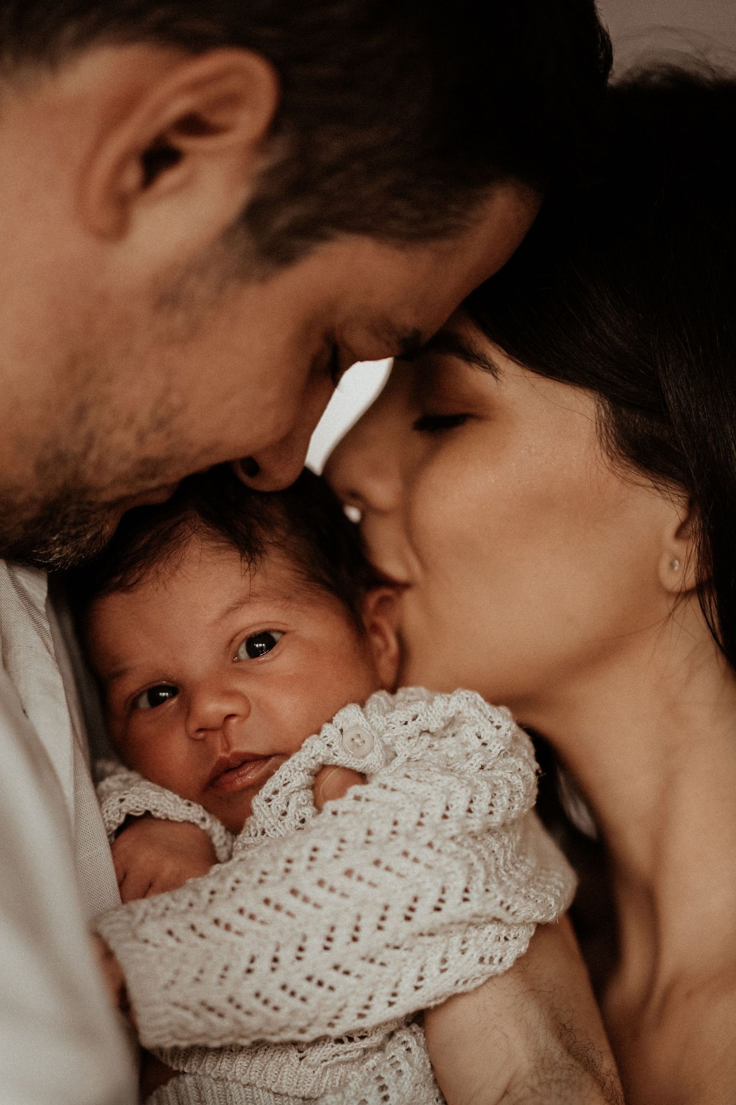 Parents cuddling their newborn close during an intimate in-home newborn photography session.