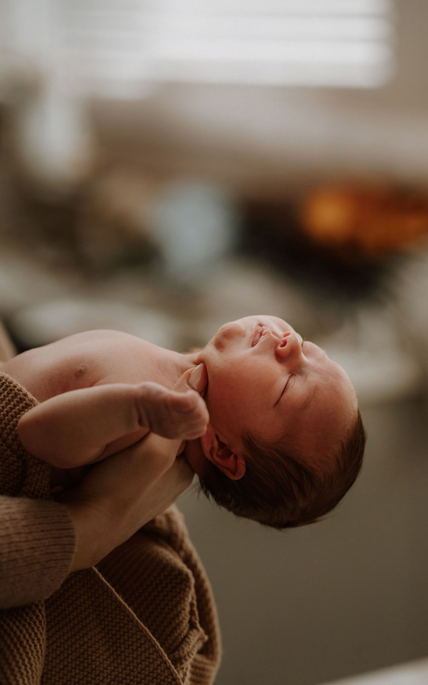Parent holding a newborn against their shoulder during a warm natural light lifestyle newborn session.