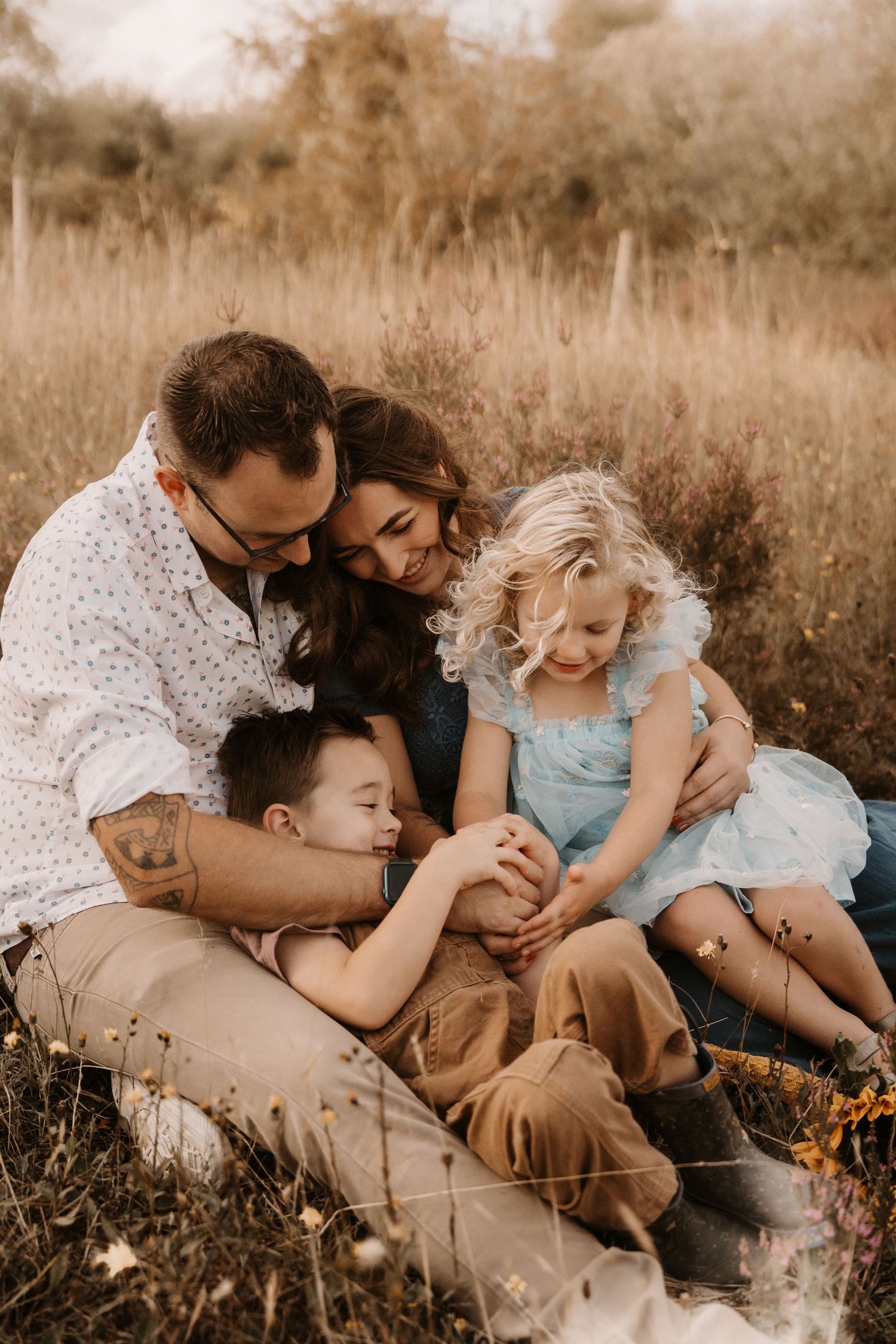 Family cuddles together in tall grass during a relaxed outdoor photoshoot in Overseal