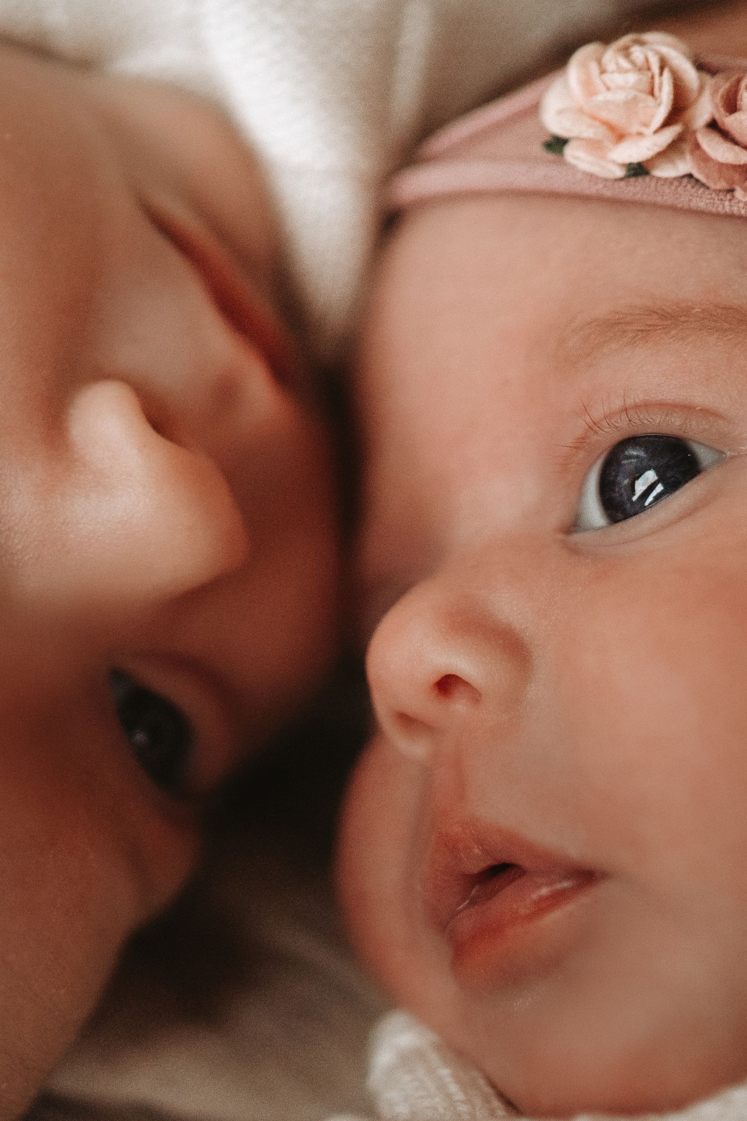 Newborn twins snuggle close together, their faces touching softly in a warm, heartfelt portrait.Natural At-Home Sessions