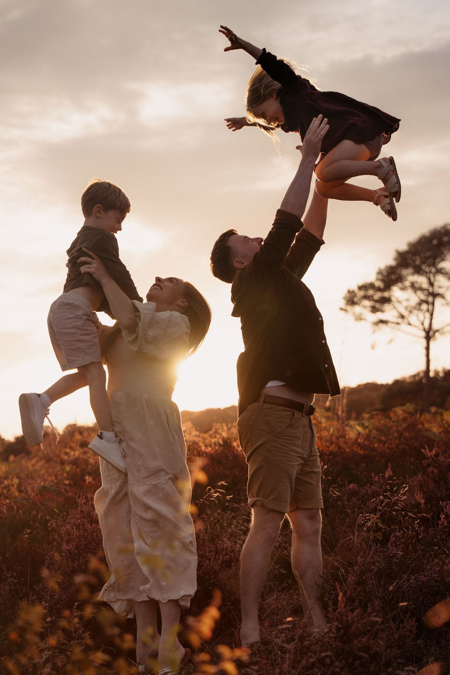 Family playing freely during holden hour, sun behind them, kids high in the sky