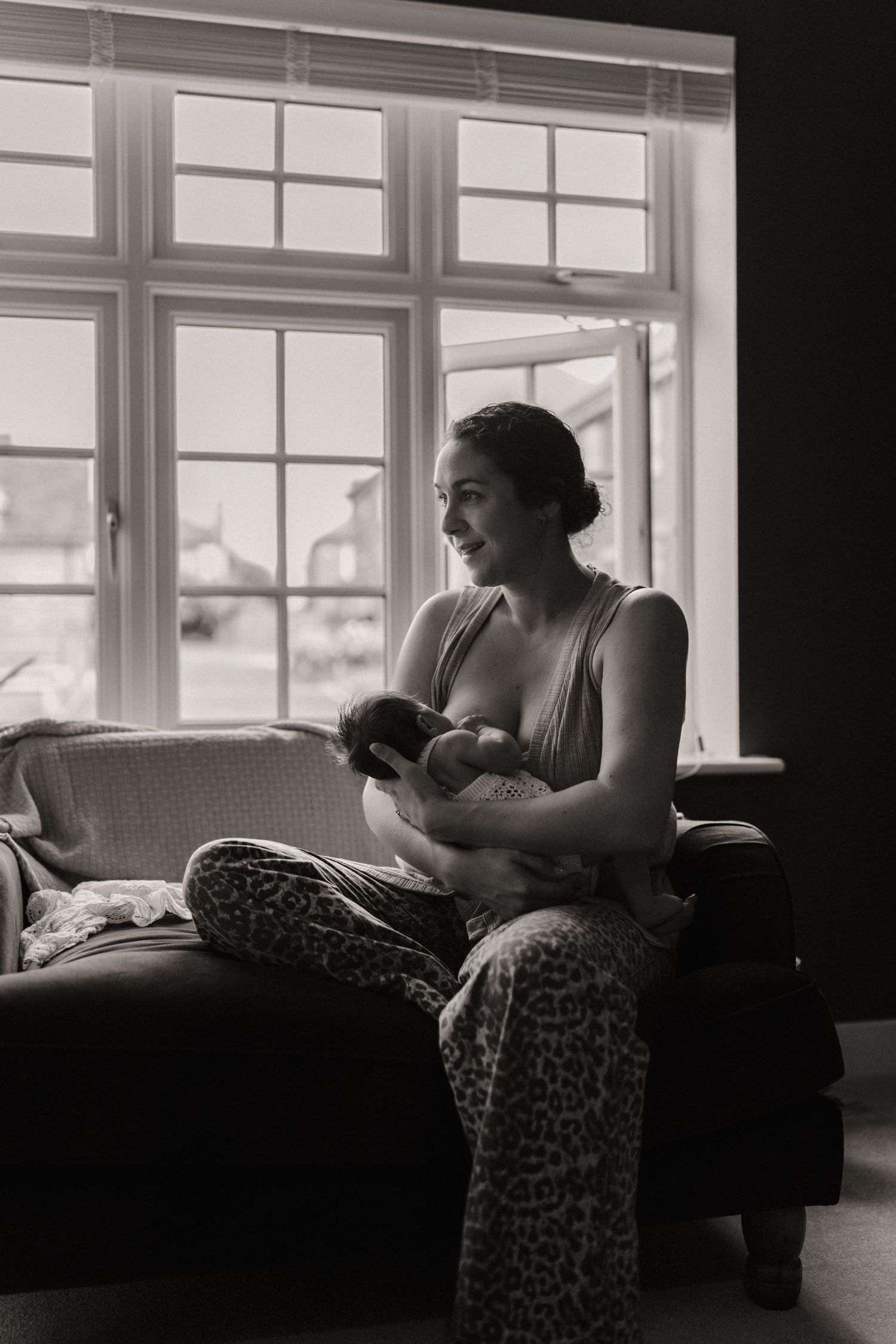 Mother nurses her newborn by the window in peaceful morning light during an at-home session in Melbourne