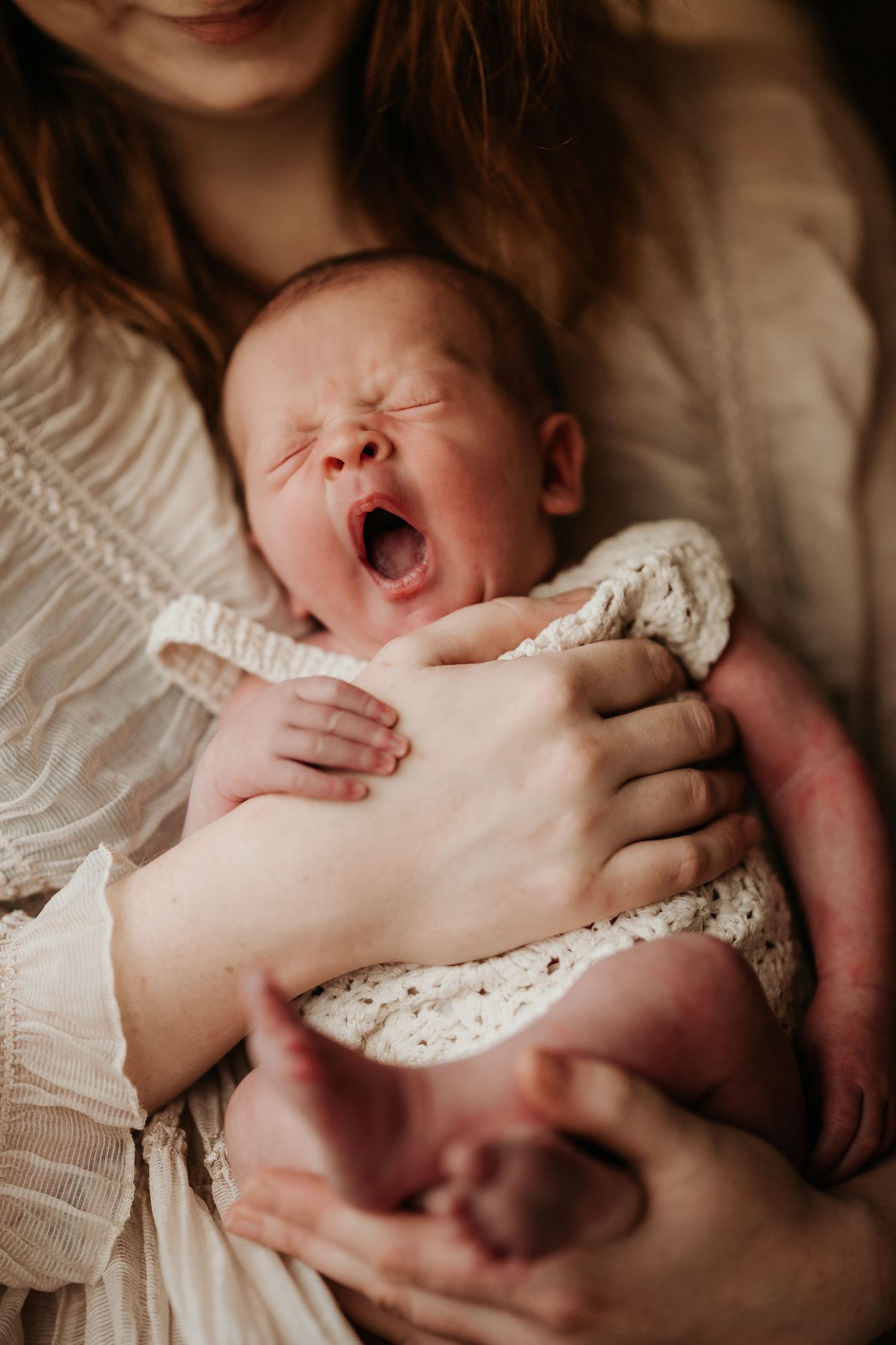 Newborn yawning in their mother’s arms, captured honestly during a relaxed storytelling newborn photoshoot.