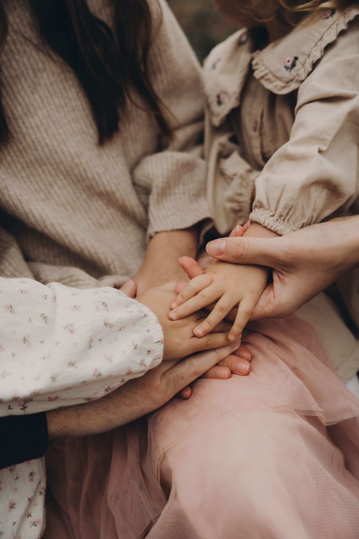 Mother and children’s hands meet gently in a warm, connected family moment outdoors.