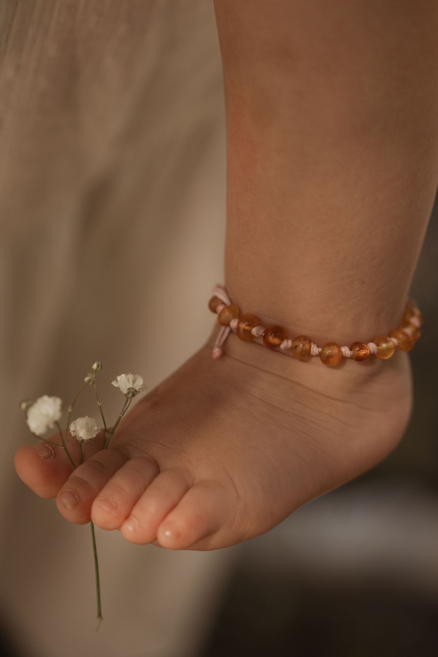 Child’s foot wearing a beaded anklet, holding a small flower during a soft lifestyle detail shot in Burton on trent