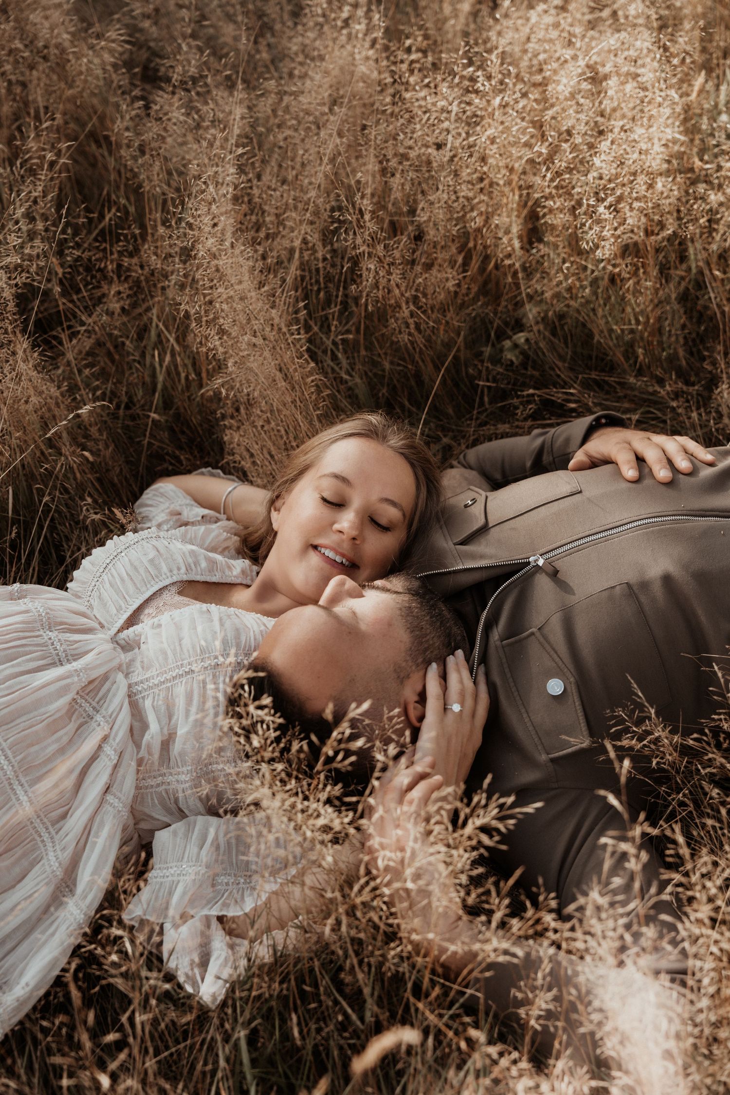 Family resting together in tall grass, holding hands during a relaxed outdoor session with Soft Stories by Angela