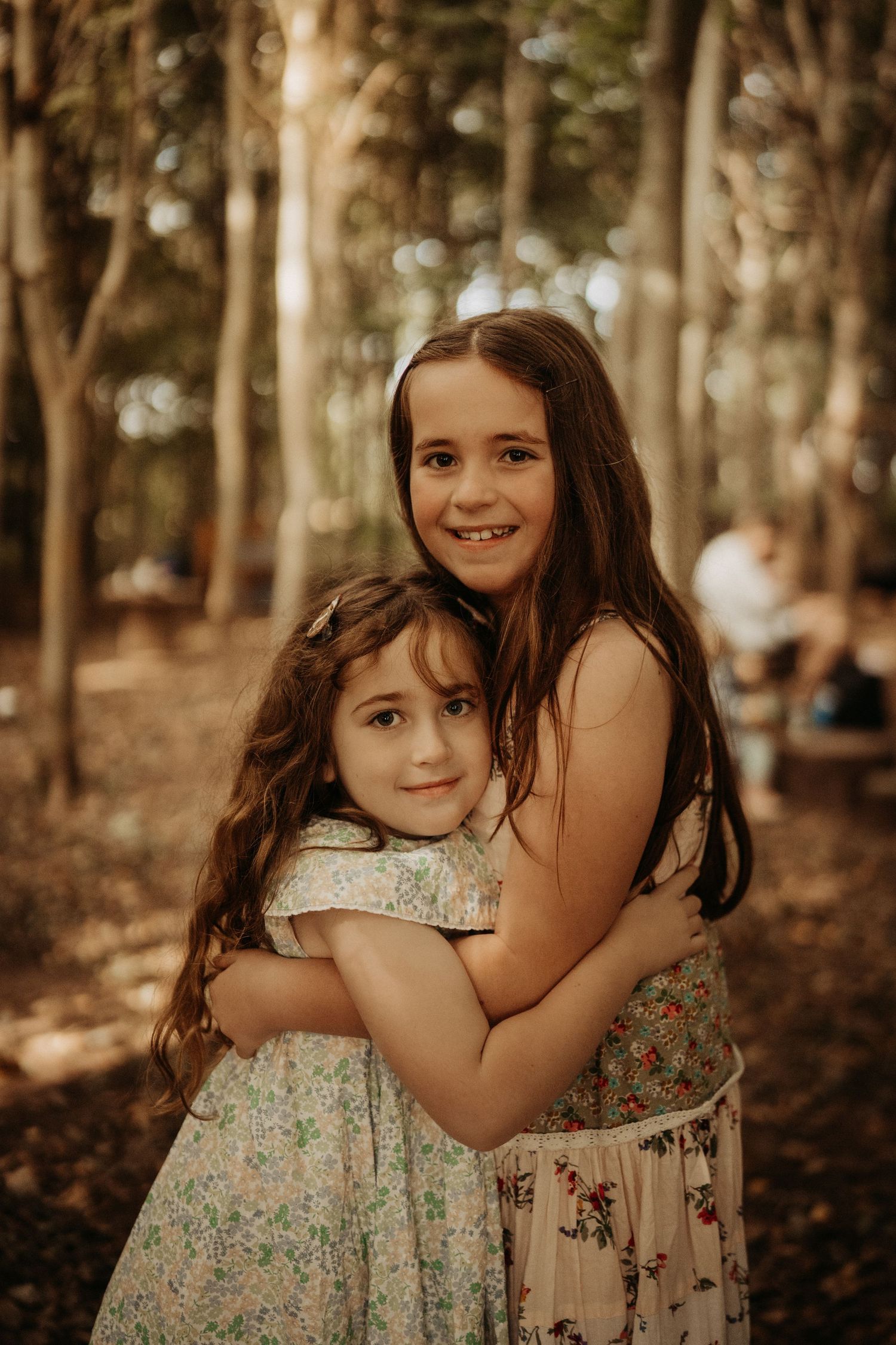 Two sisters hugging in a woodland clearing during a candid outdoor photoshoot at Little Wildlings Natureplay