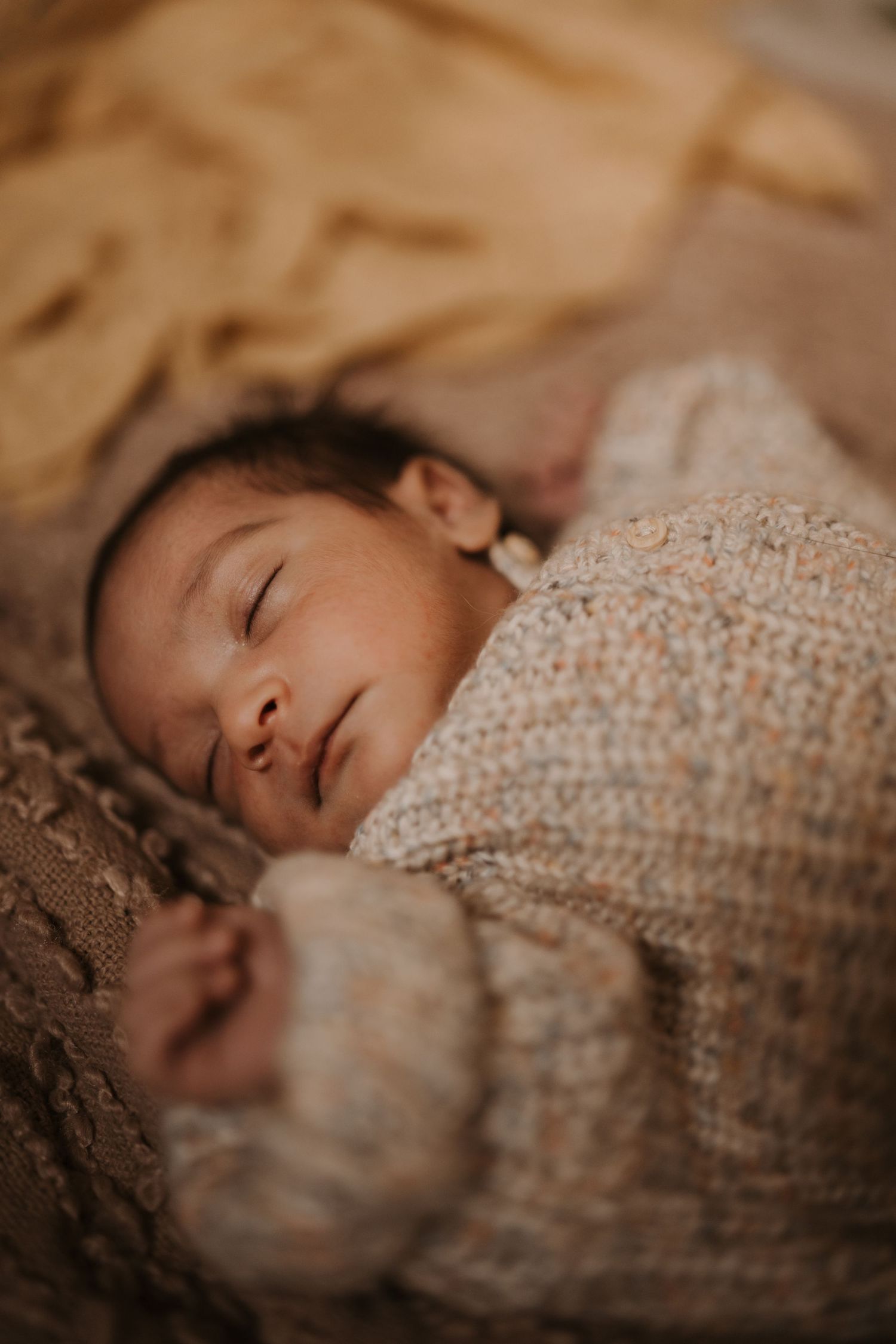 Sleeping newborn wrapped in soft textures during a cosy storytelling newborn photoshoot.