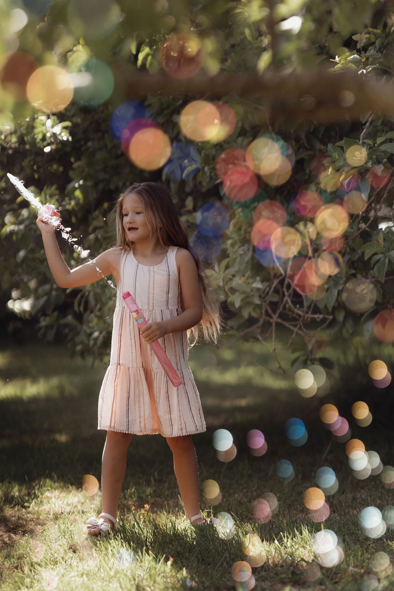 Child standing outdoors blowing bubbles in a garden by Soft Stories by Angela