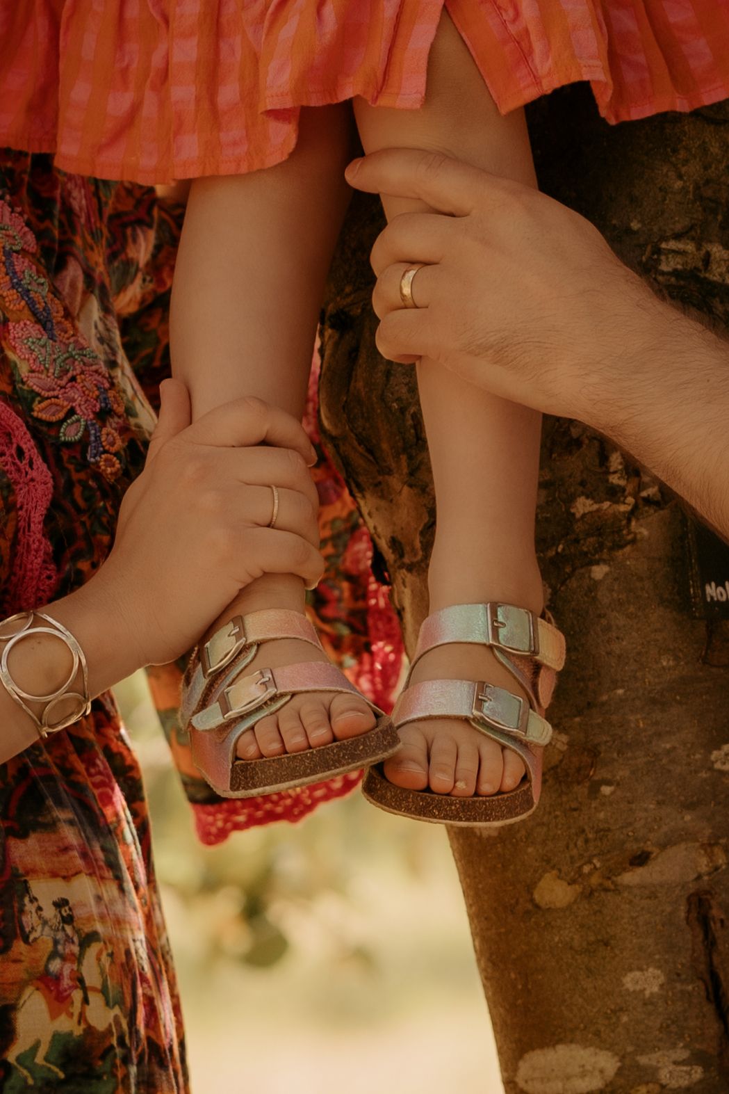 Close-up of small feet in sandals, gently held by an parents hands in summer warmth during storytelling maternity shoot in Calke Abbey