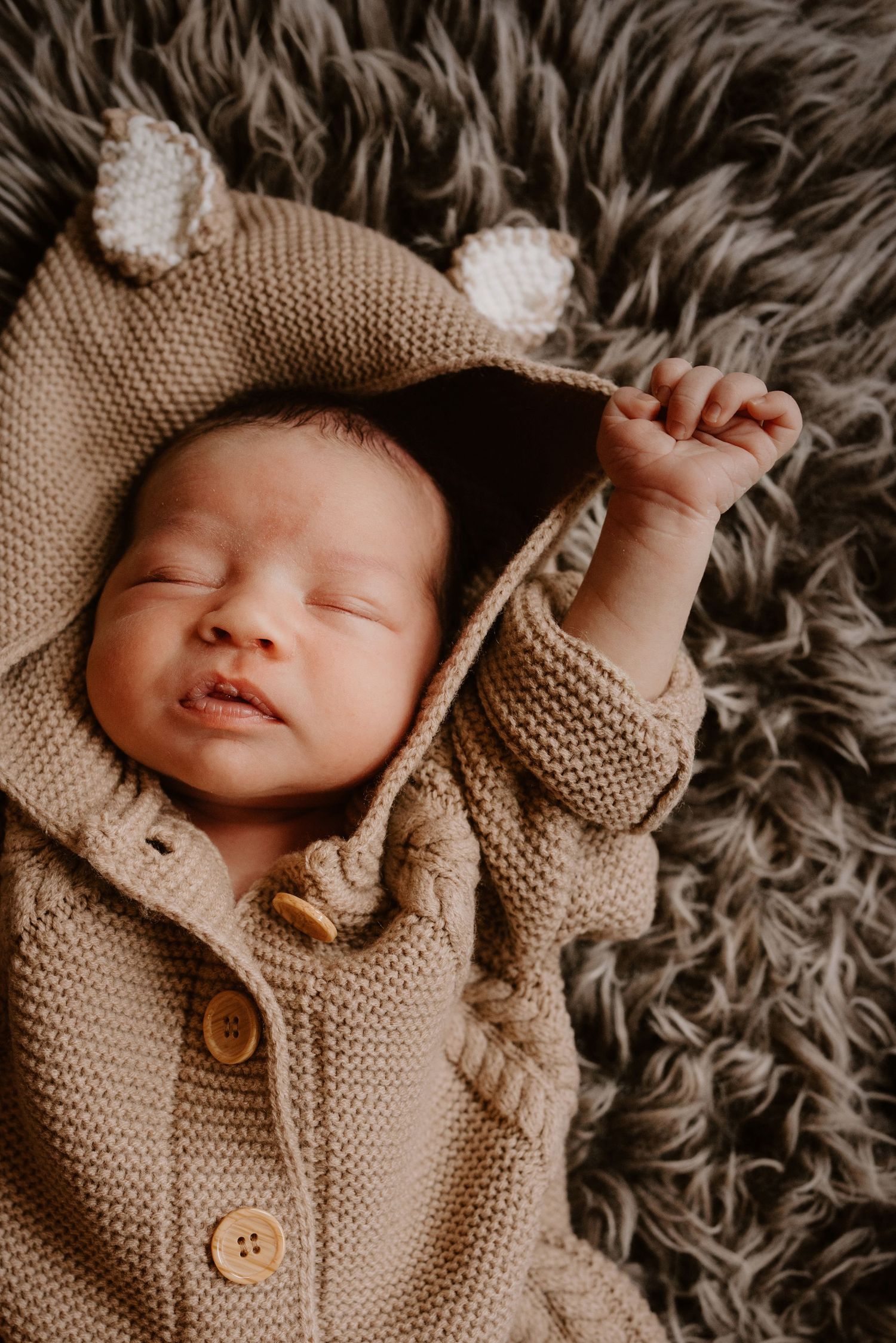 Newborn stretching in a knitted outfit during an in-home natural light lifestyle newborn photography session in Swadlincote