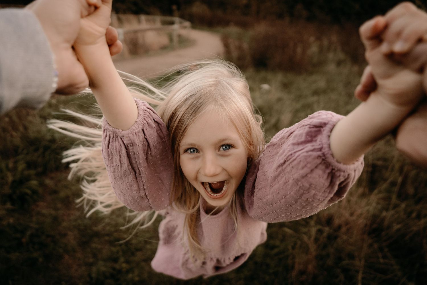 Child laughing while being swung by their arms during a joyful outdoor documentary family photoshoot in Swadlincote