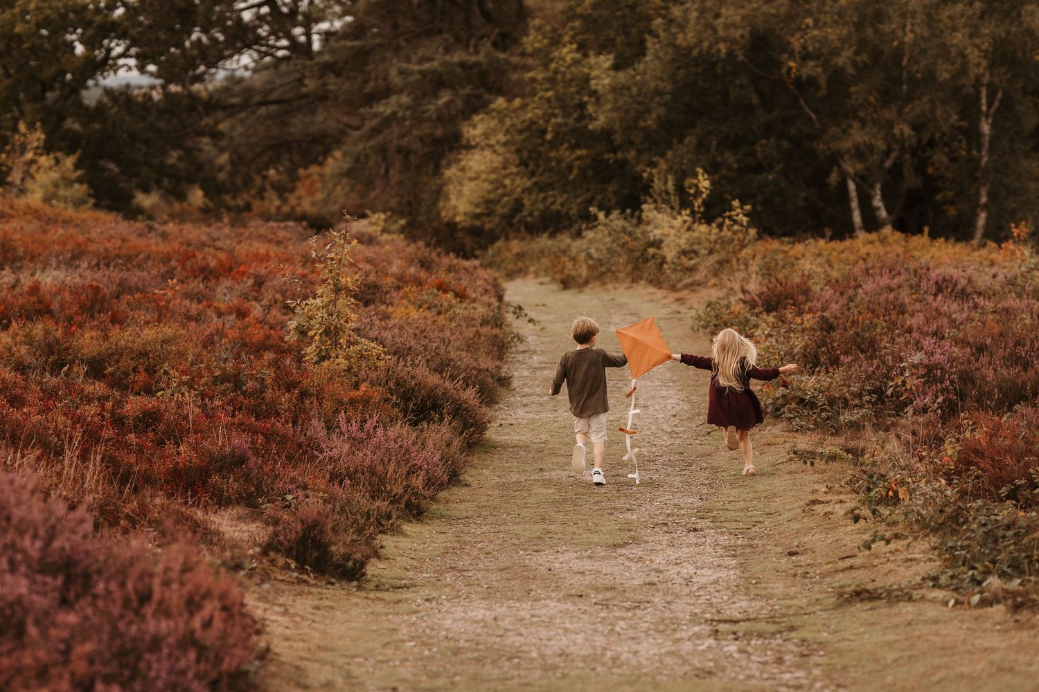 Kids run with orange kites through autumn paths during a playful Lickey Hills photoshoot.