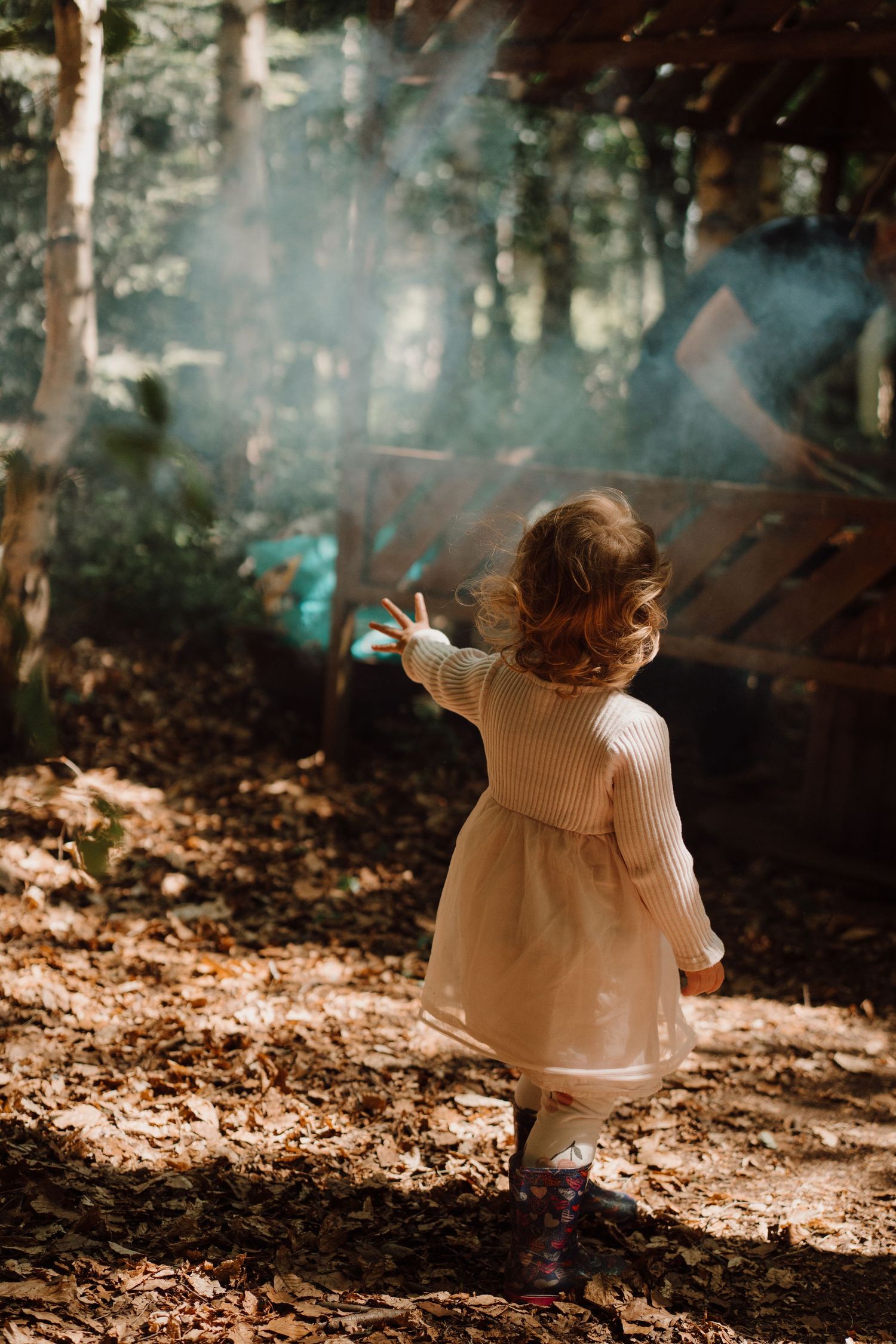 Little girl walks through woodland light and smoke during a dreamy storytelling photoshoot outdoors in Little Wildlings Natureplay